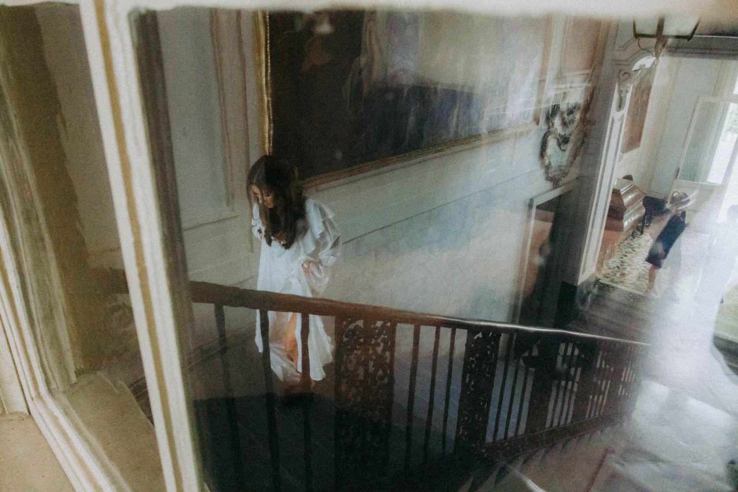 A blurry vintage photograph shows a person standing at the top of a dark staircase in a dimly lit hallway.