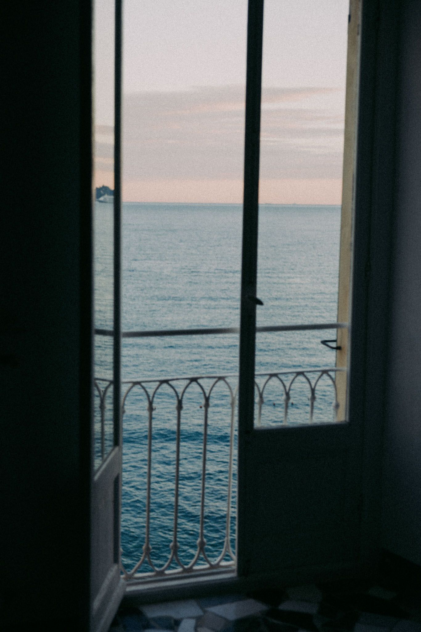 View of calm ocean waters through a window with ornate railing at sunset, creating a serene coastal atmosphere.