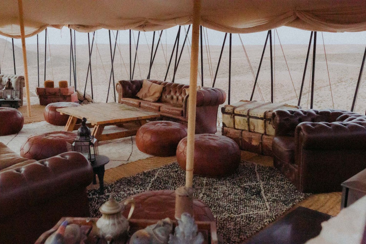 Cozy glamping interior with plush furnishings and rustic decor inside a luxury tent in a desert setting.