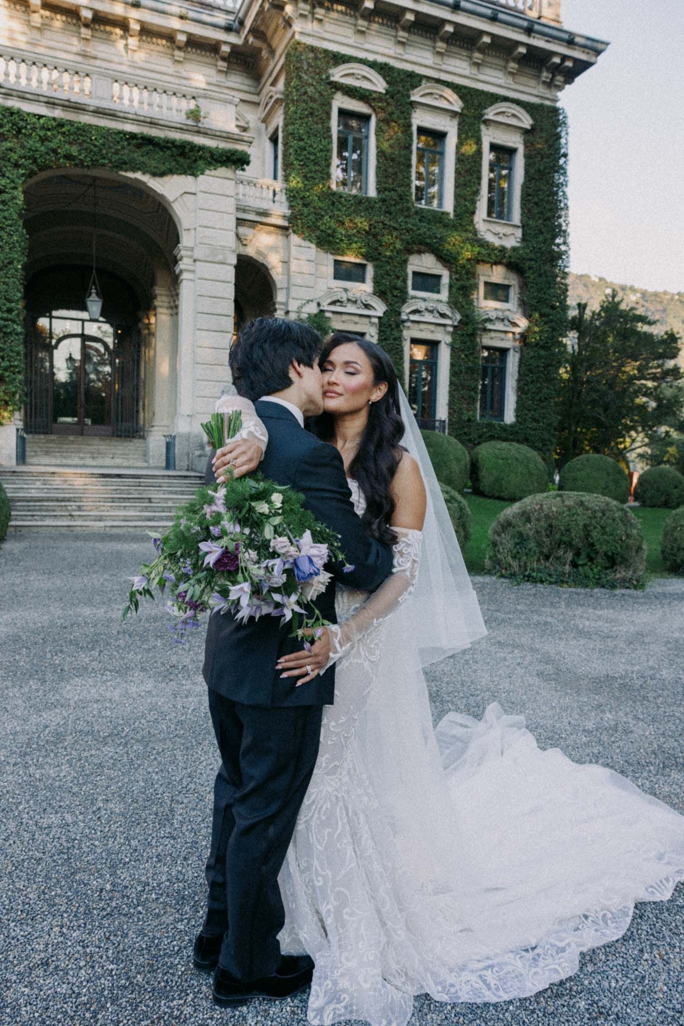 Romantic wedding moment captured outside grand historic estate with ivy-covered walls.