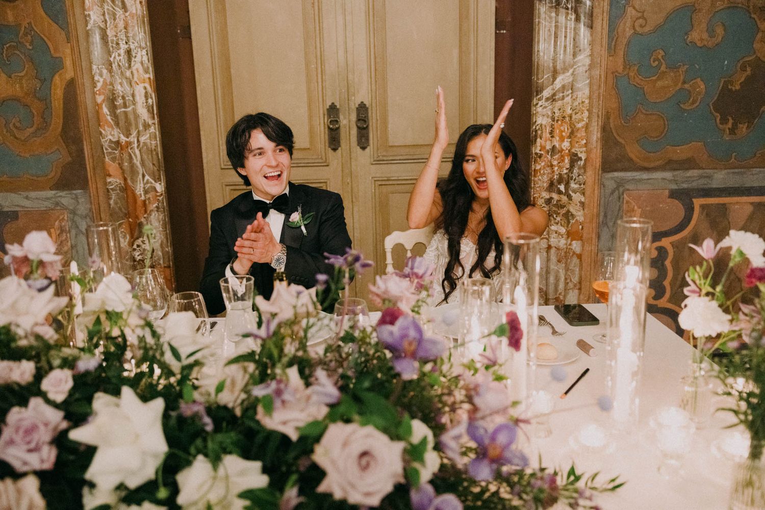 Elegant wedding reception table setting with pink and white floral centerpieces in an ornate ballroom with gold details.