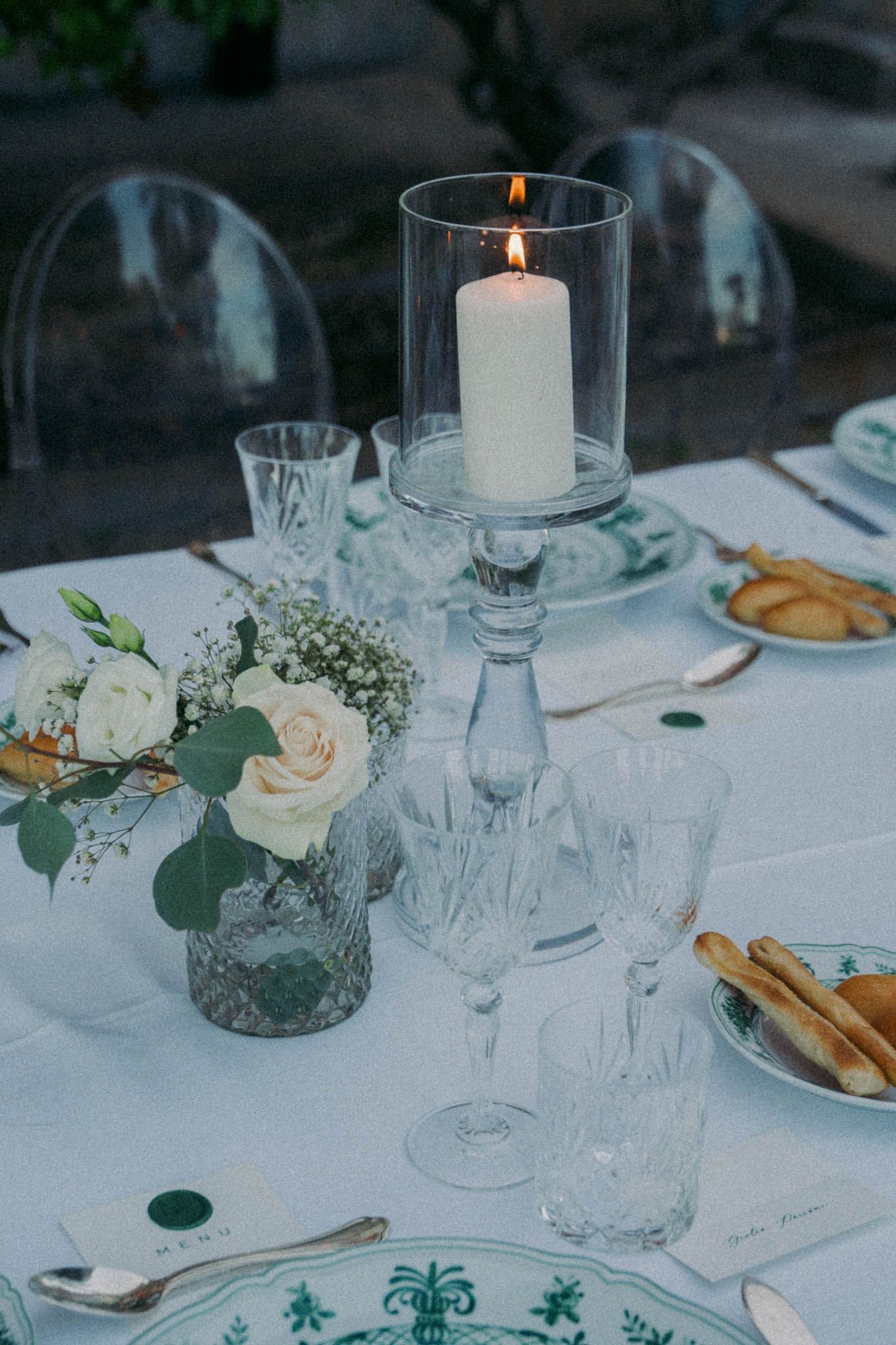 Elegant wedding table setting with white candles, roses, and glassware on crisp white tablecloth.