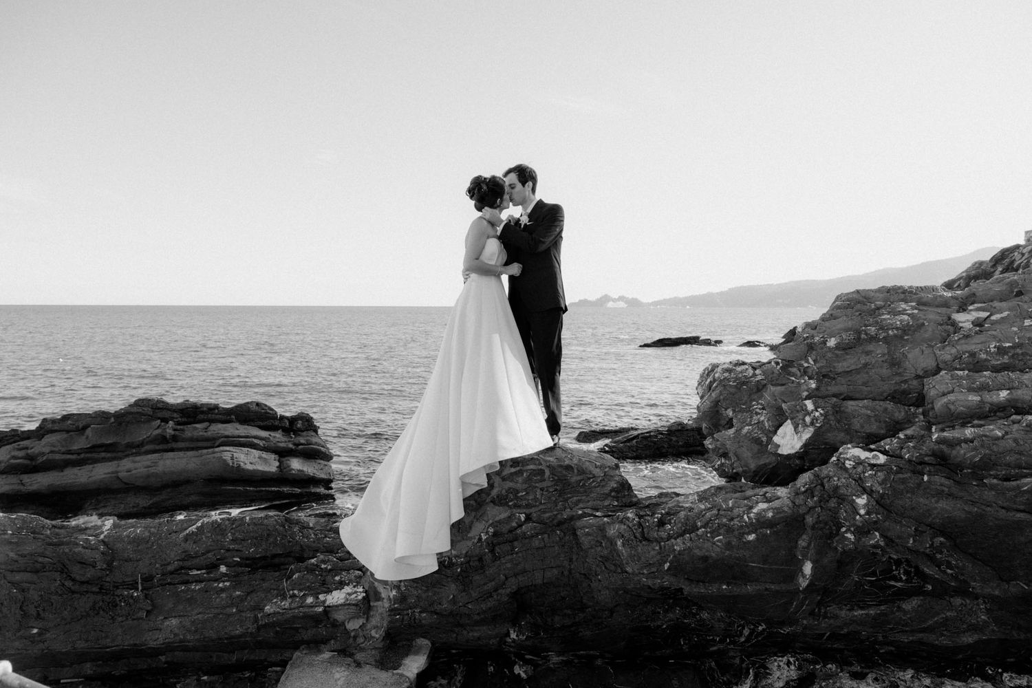 Dramatic black and white wedding photos captured along rocky coastal cliffs.