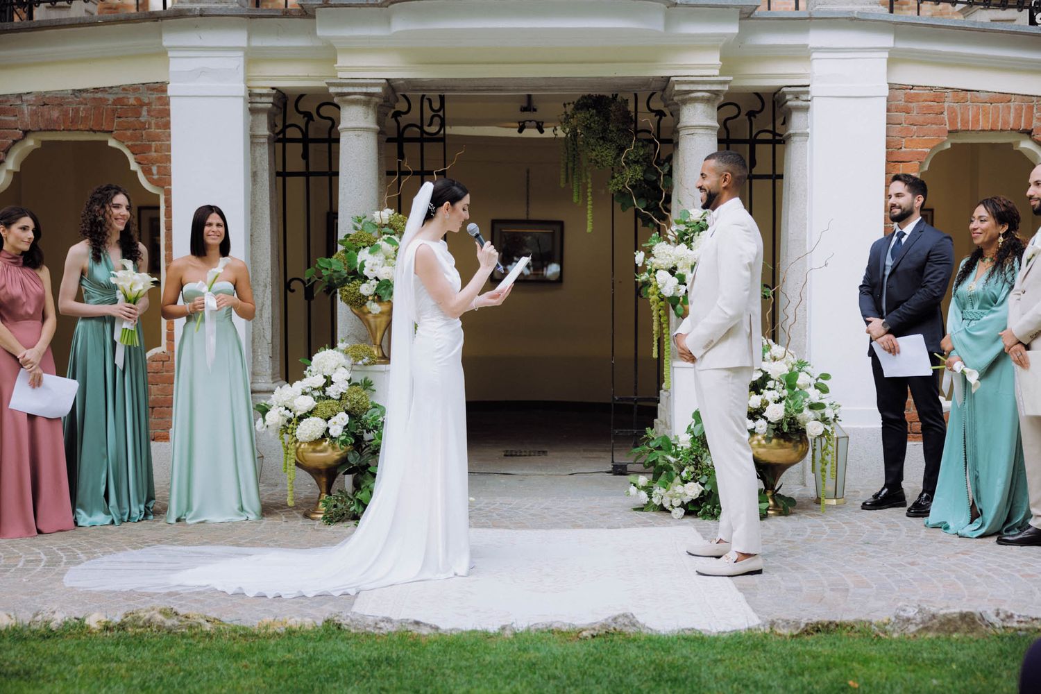 Wedding party members in mint green dresses and dark suits pose together for formal portraits on church grounds.