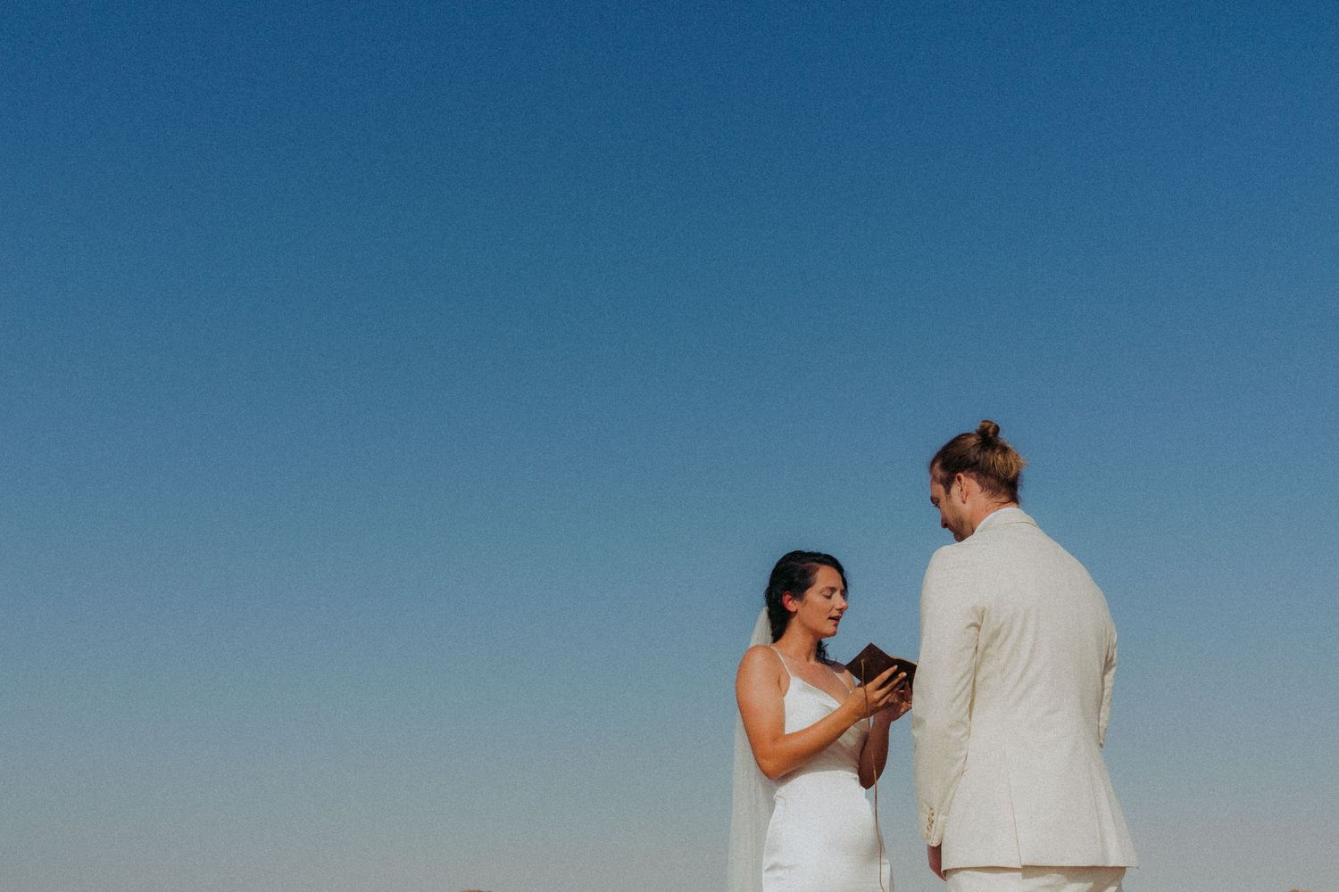 A couple stands together on a beach at sunset during their wedding ceremony.