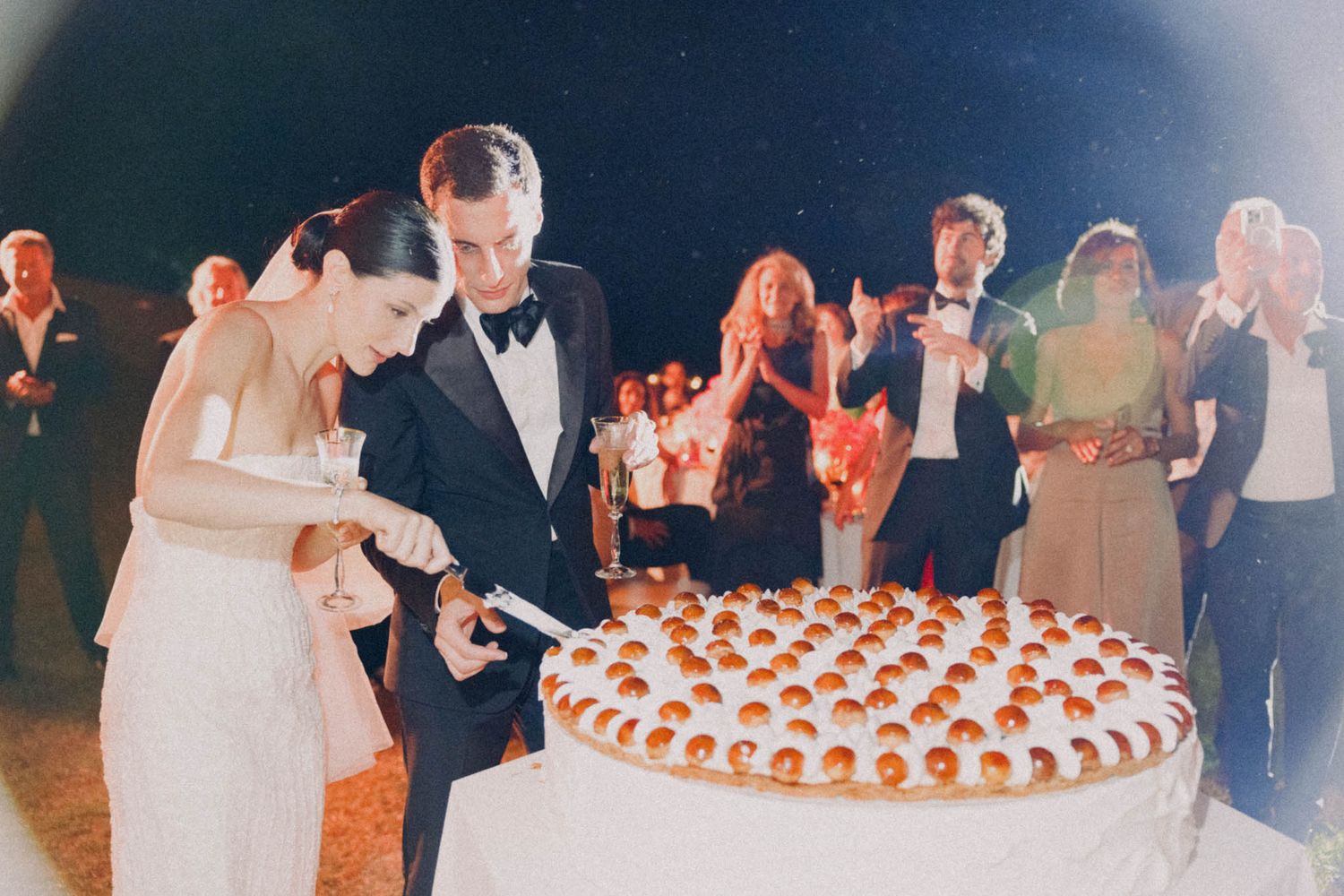 Wedding guests gather around a tiered dessert display at an elegant evening reception.