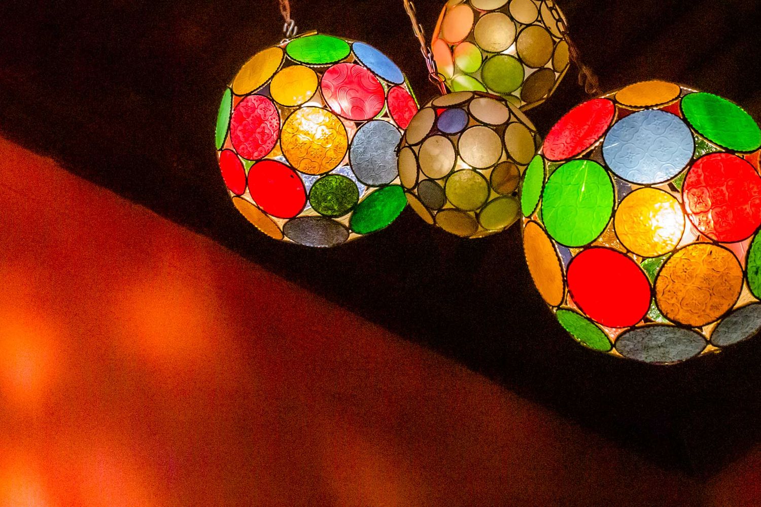 Colorful stained glass mosaic lanterns glowing with warm light against a dark red background.