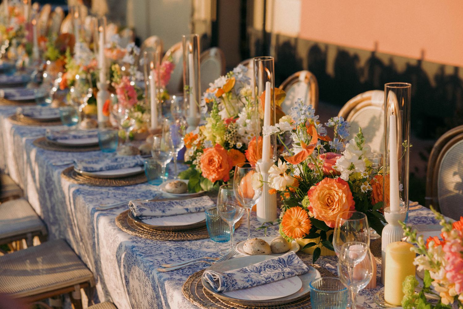 Elegant table setting with orange floral centerpieces, blue linens, and glowing candles for an autumn wedding reception.