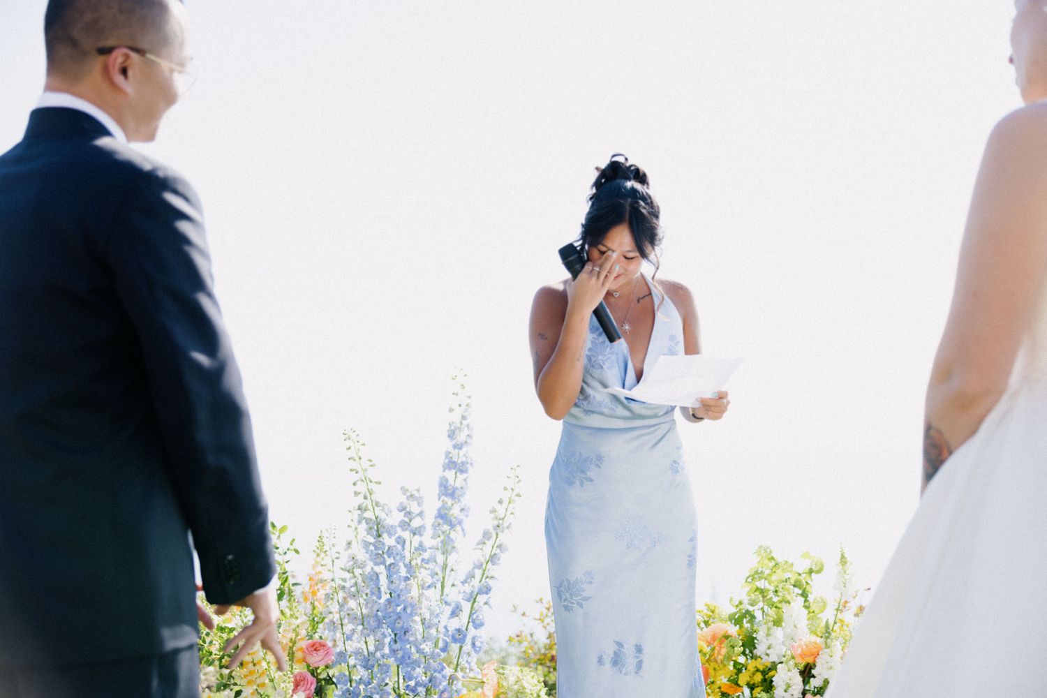 A couple in formal wedding attire poses together in a garden setting with blue flowers in the background.