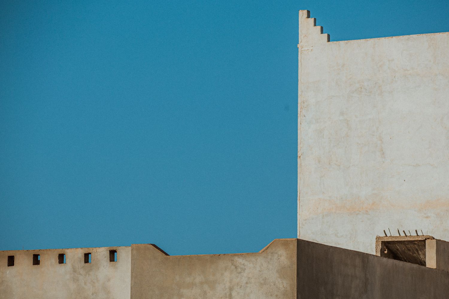 Modern architectural facade with white walls against vibrant blue sky creating strong geometric shapes.