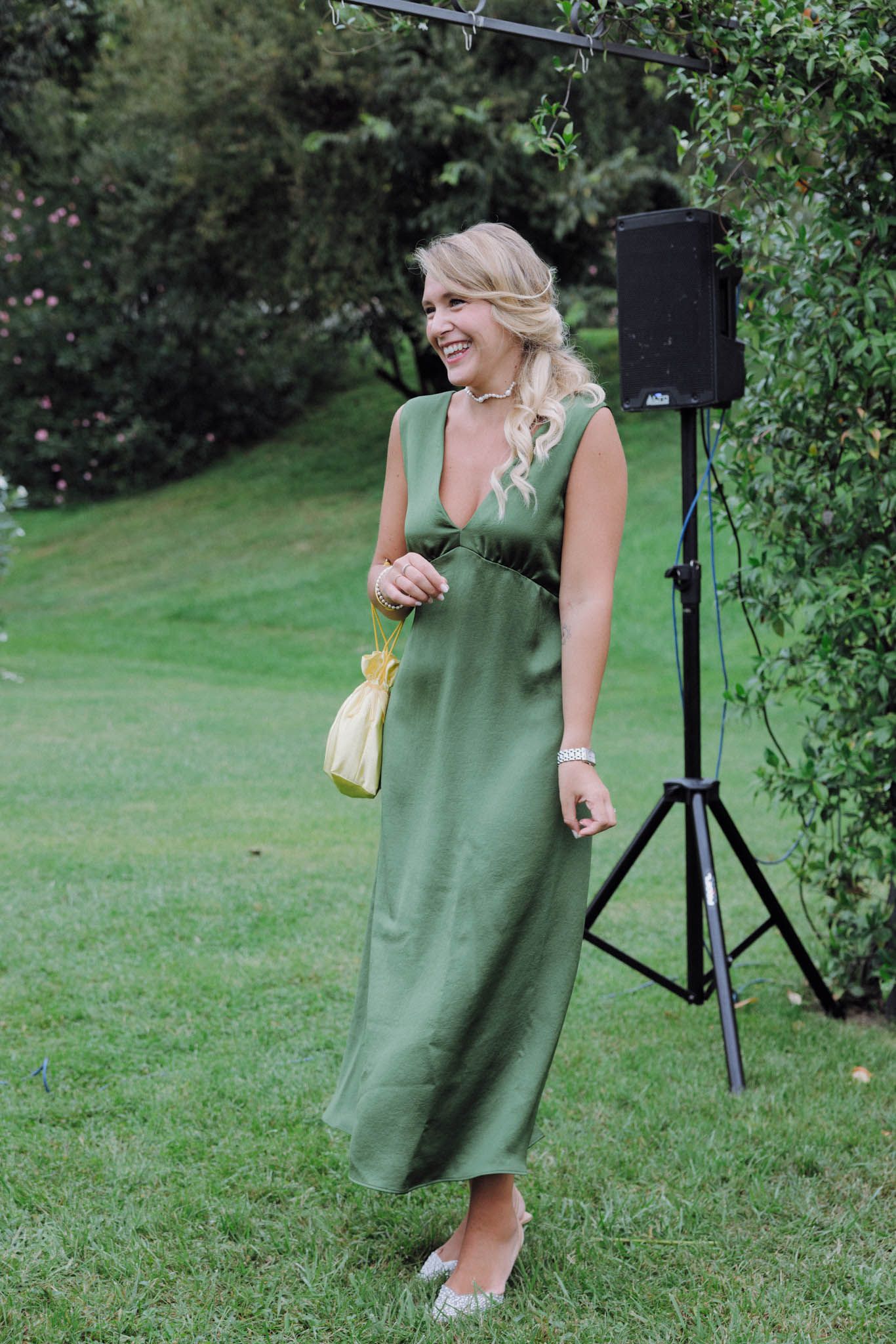 Woman in green dress poses playfully on grassy lawn with outdoor lighting equipment visible.
