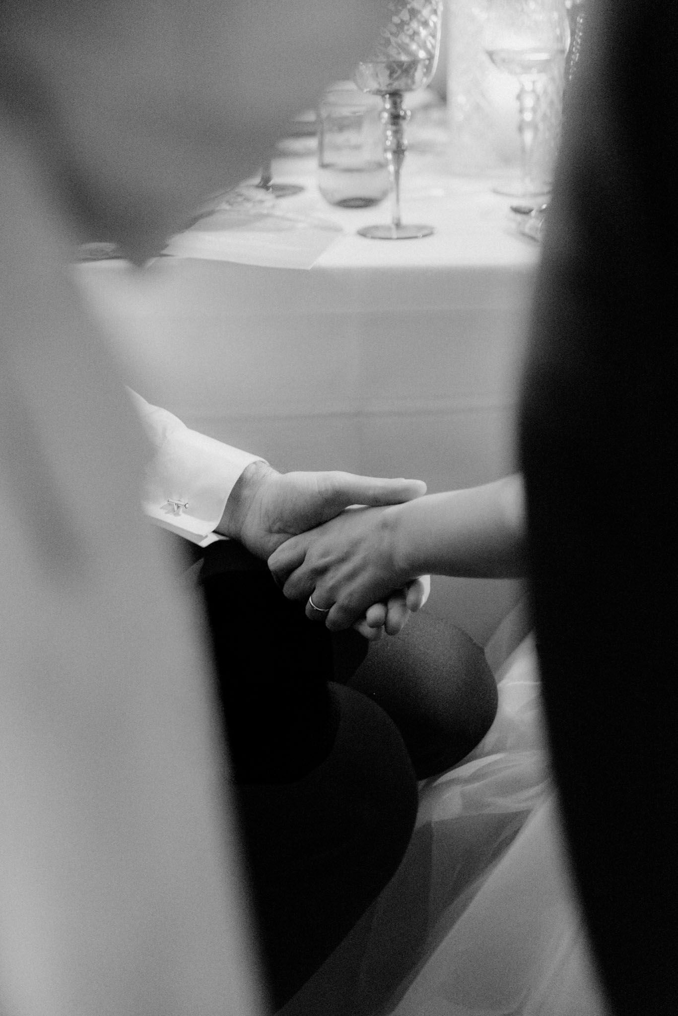 Black and white close-up image of hands holding wine glasses in a dimly lit setting.