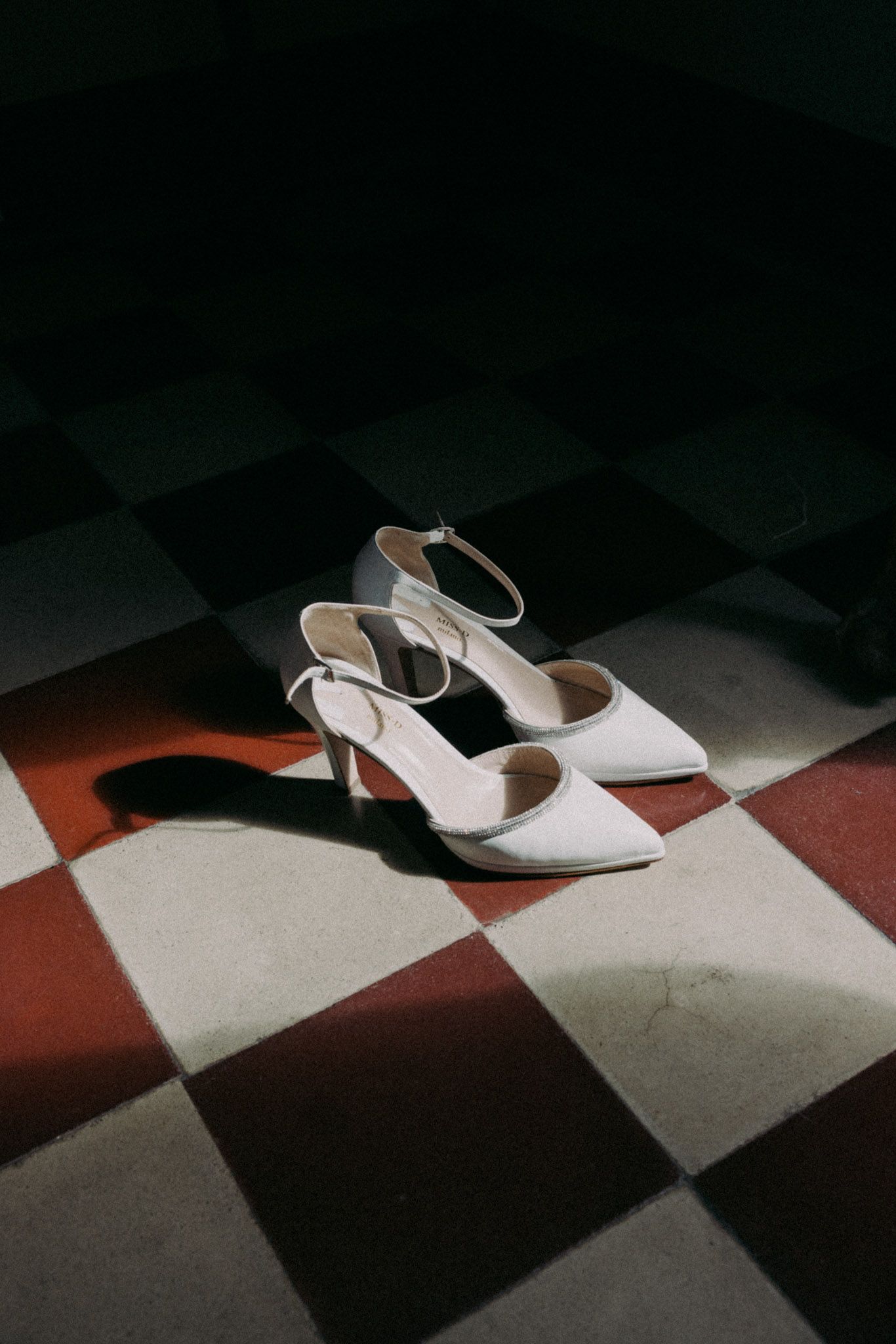 White high heeled shoes on a black and white checkered floor create dramatic shadows and lighting effects.