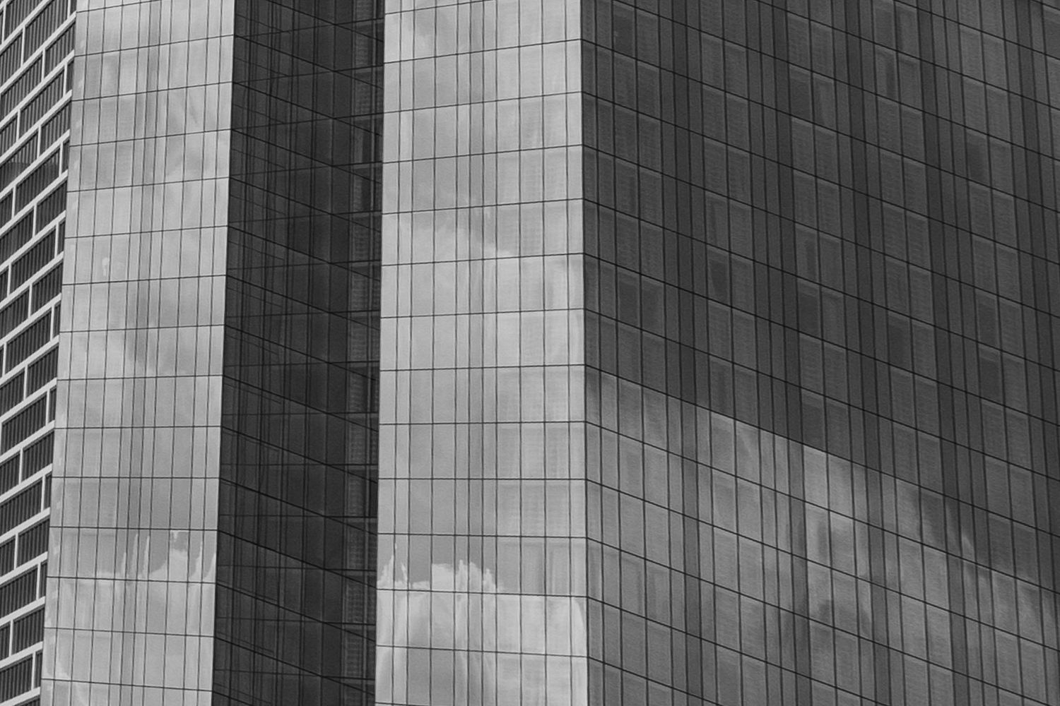 Modern glass office building facade with geometric pattern of reflective windows and dark vertical lines.