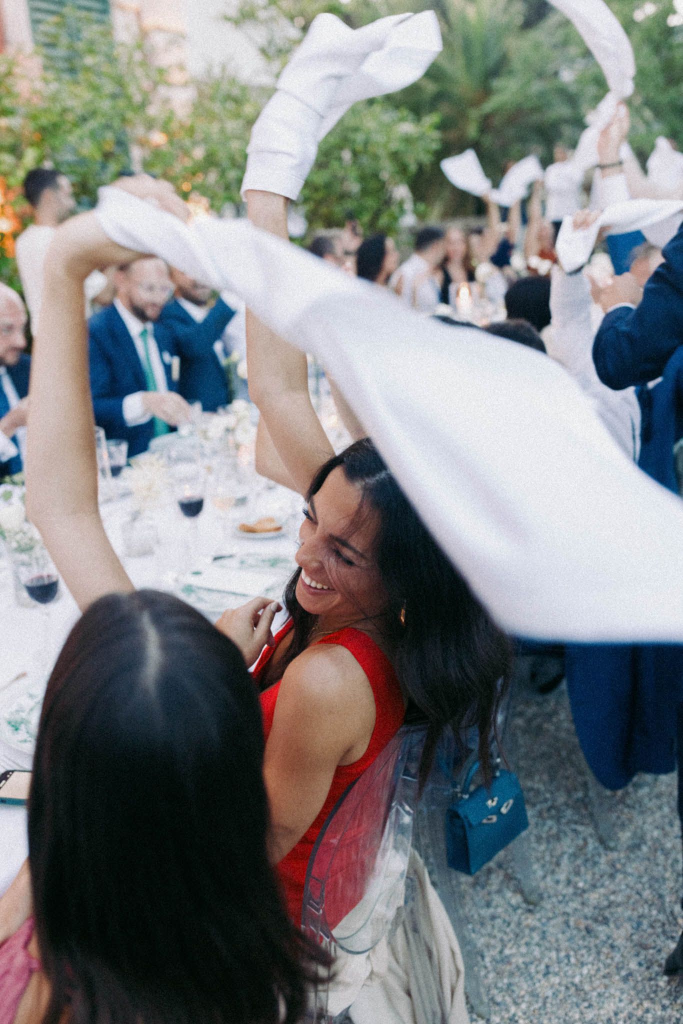 Wedding guests wave white napkins in celebration during an outdoor reception gathering.