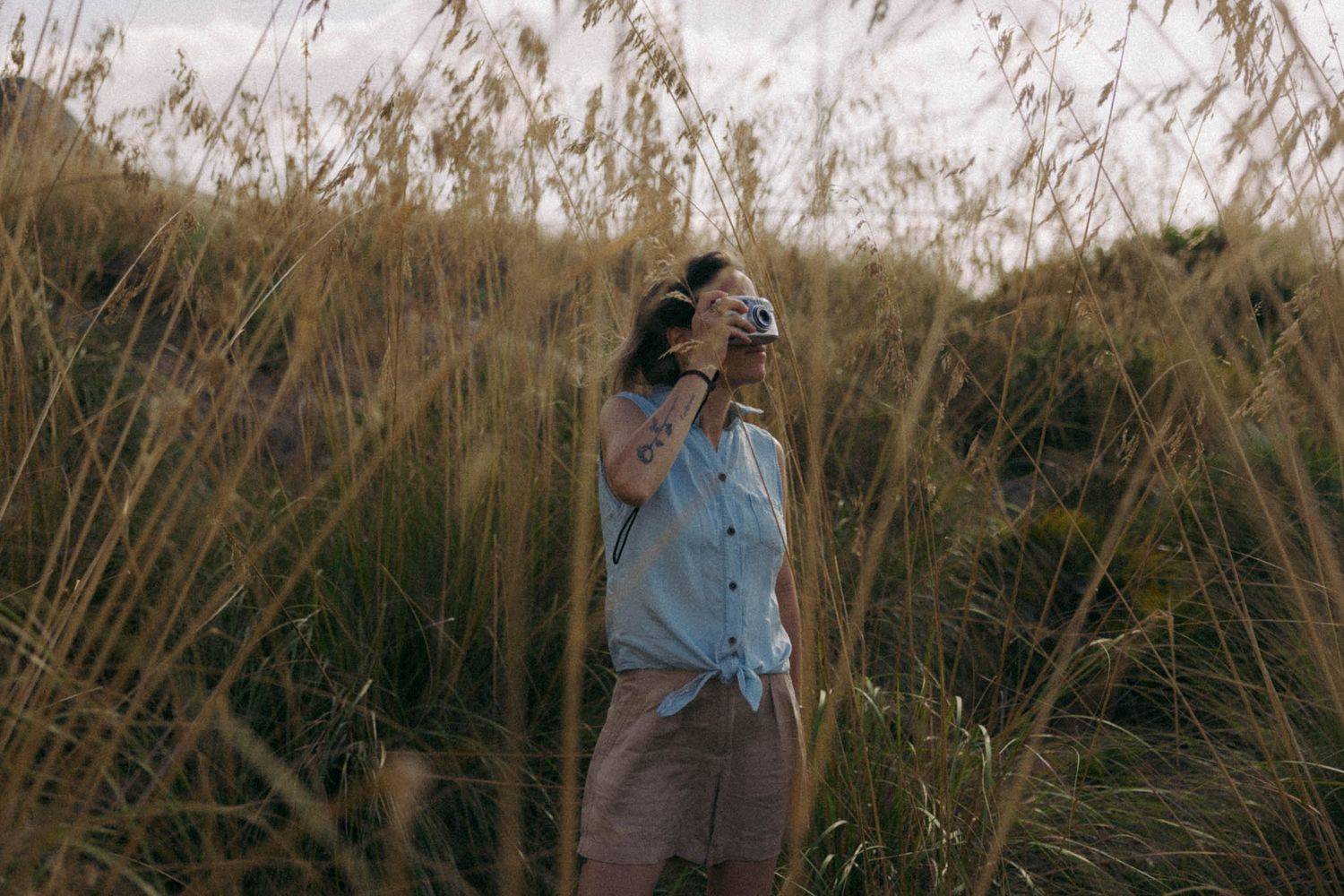 A person walks through tall golden grass in a field during sunset creating a dreamy silhouette effect.
