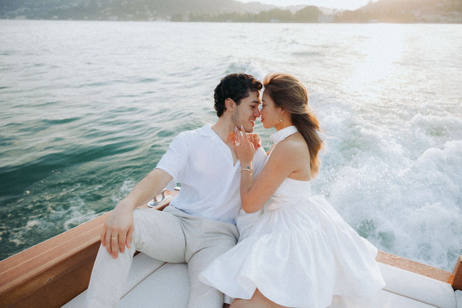 A romantic boat ride scene with a couple in wedding attire embracing on the water at sunset.