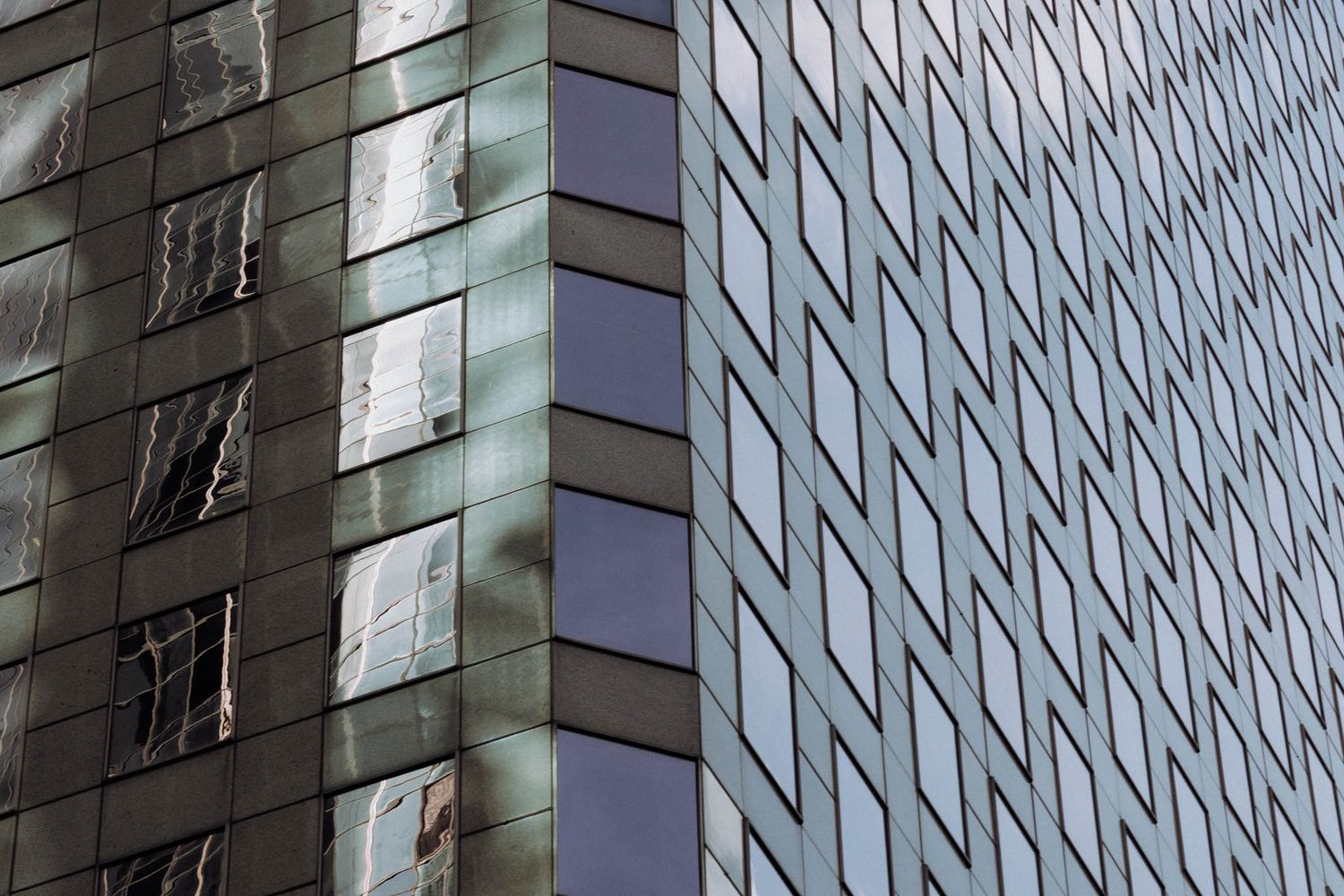 Modern glass office building facade with geometric pattern of reflective windows and metallic panels creates abstract design.