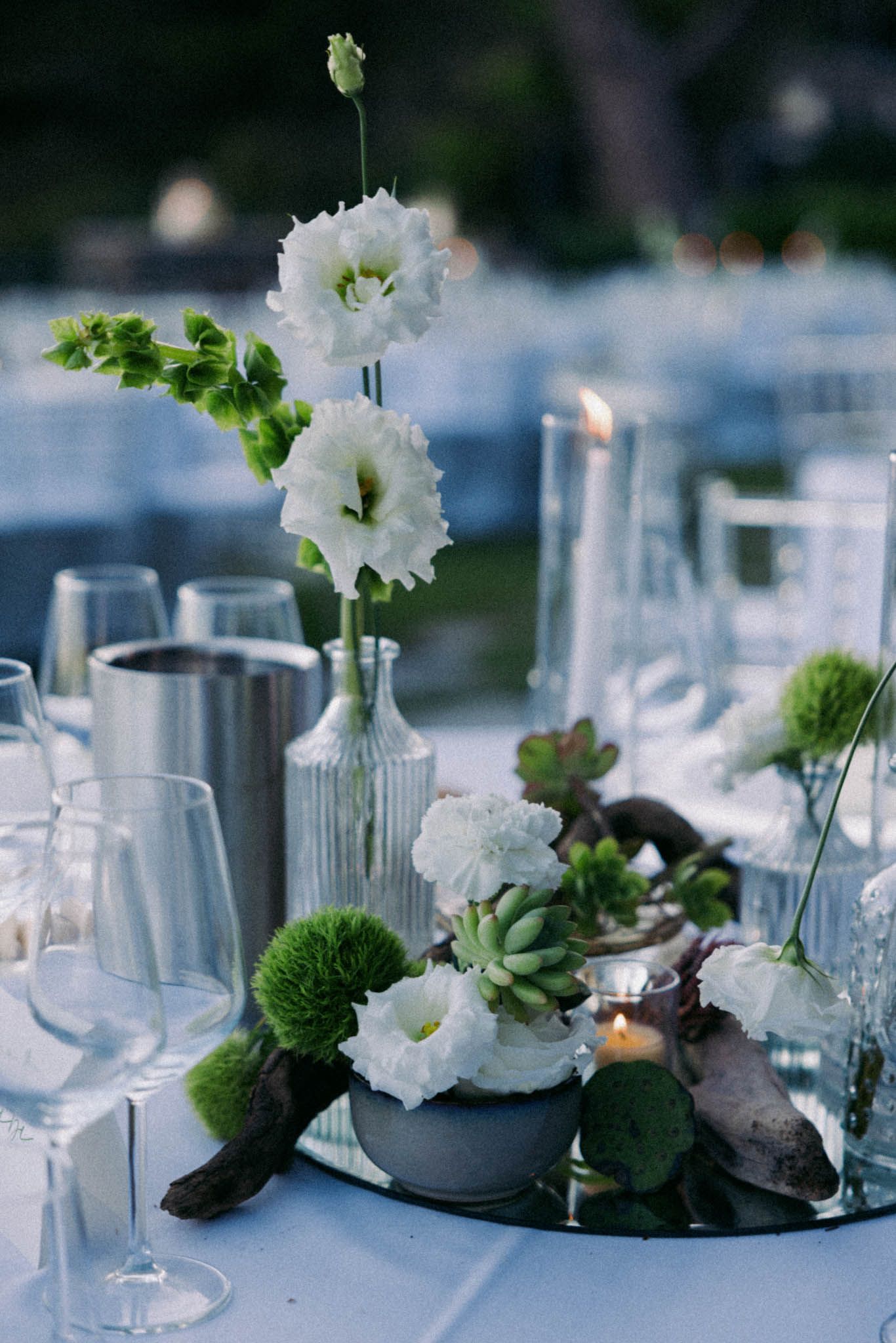 Elegant table setting with white delphinium flowers and green moss in glass vases on a light blue tablecloth.
