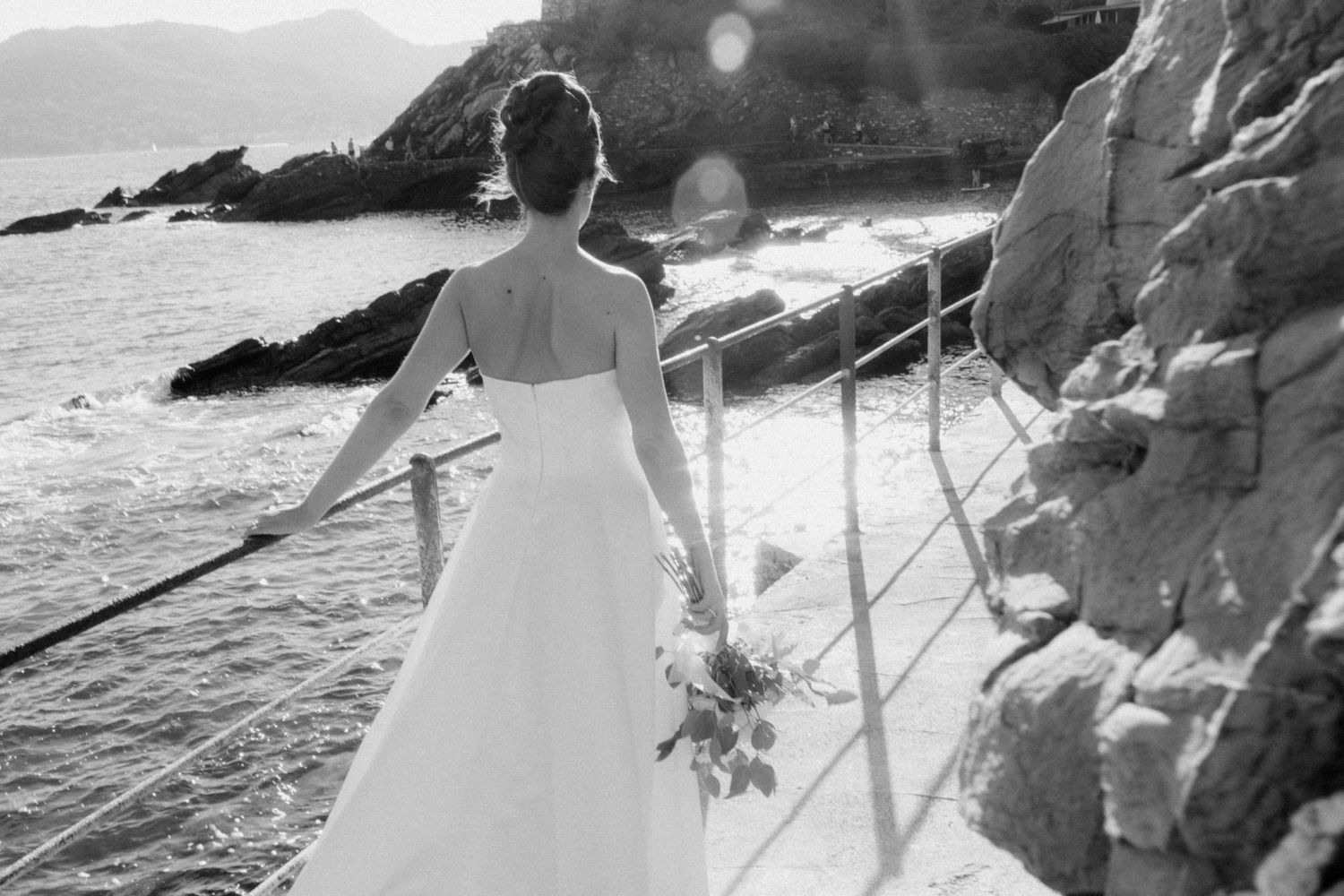 Black and white beach wedding photos showing couple walking along rocky coastline at sunset.