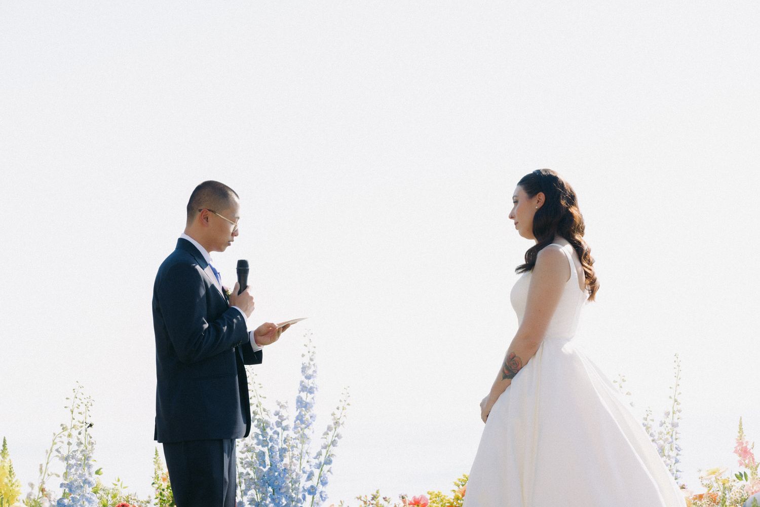 Wedding ceremony takes place outdoors with mountains and blue sky in the background.