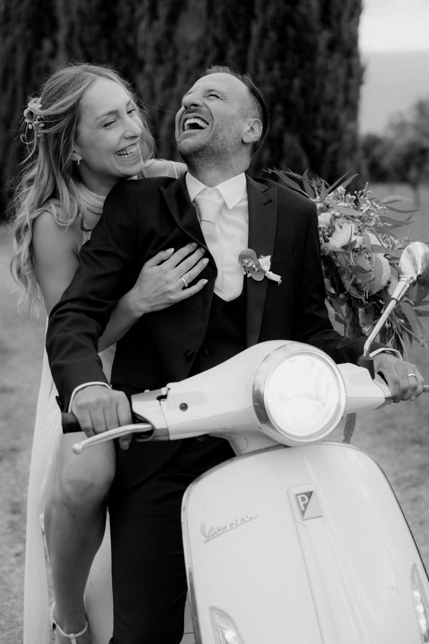 A couple shares joyful moments together with a white Vespa scooter in a series of black and white wedding photos.