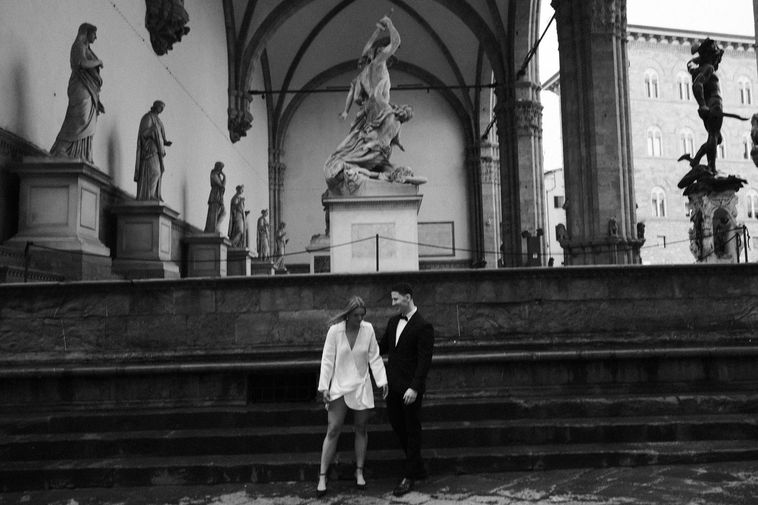 Black and white photos of figures walking among classical statues and architecture.