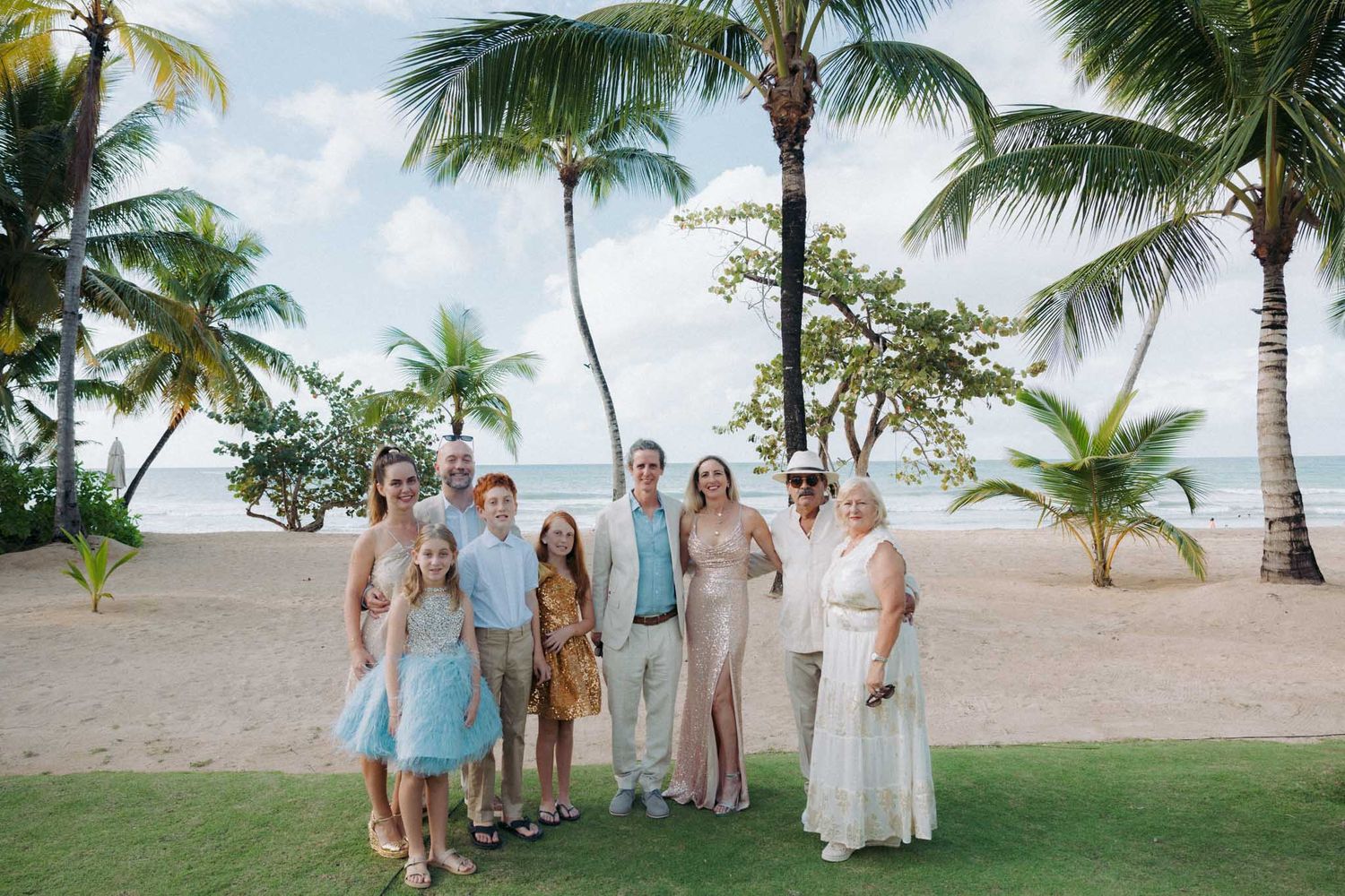 A group stands together on a tropical beach with palm trees and white sand under a bright blue sky.