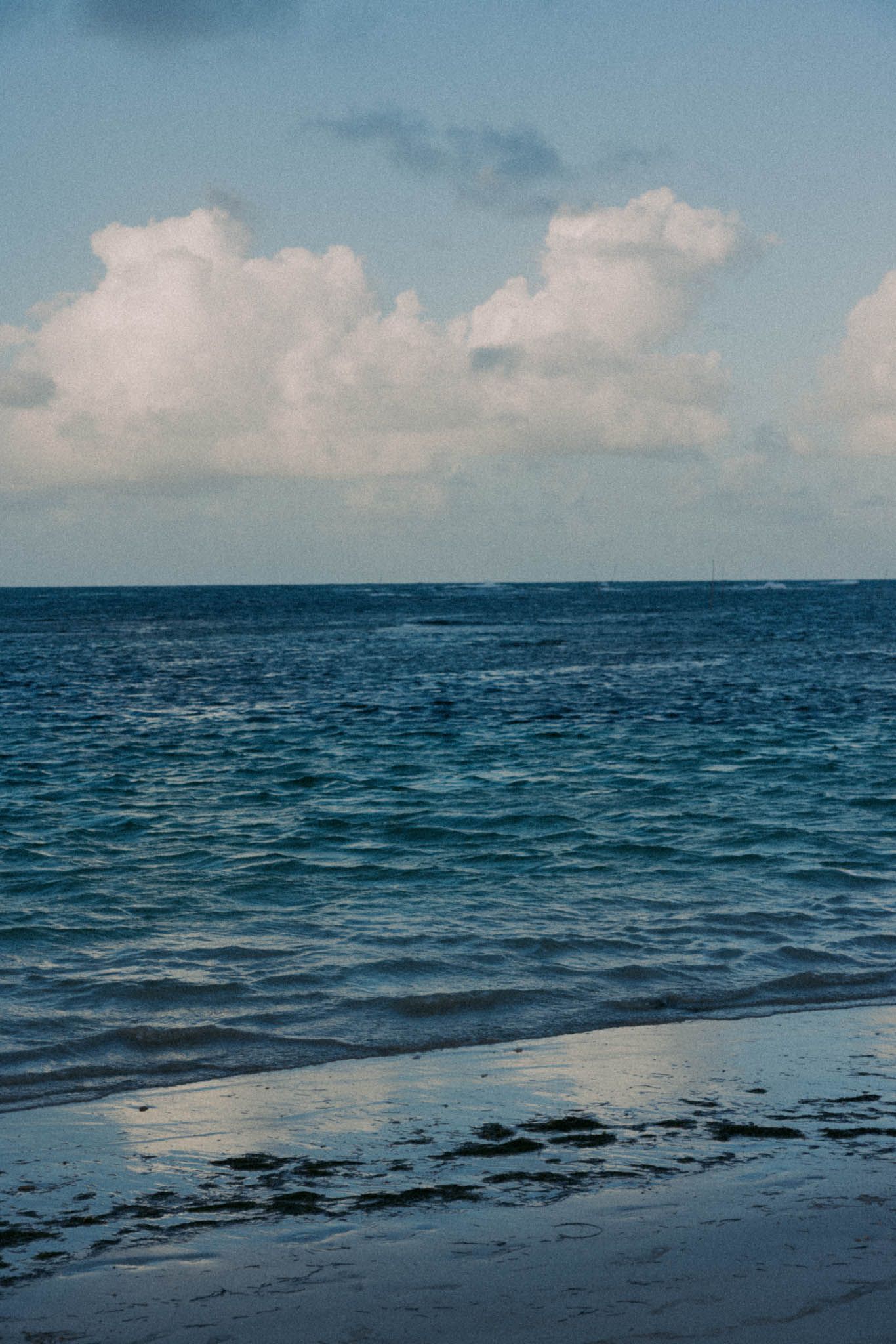 Serene ocean view with dark blue waters meeting a sandy beach under cloudy skies.