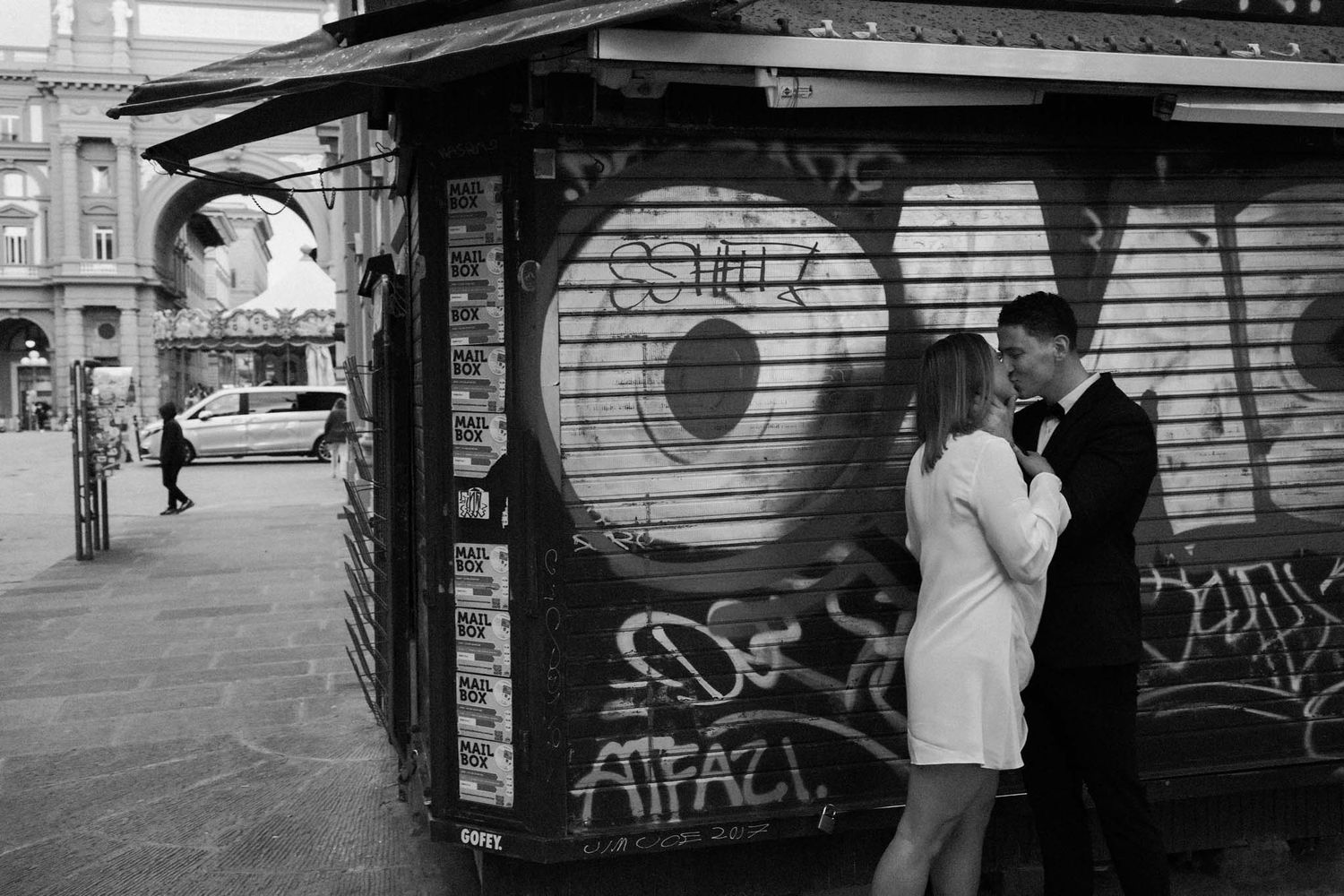 Panoramic black and white urban scene showing people near graffiti-covered walls and metal shutters.