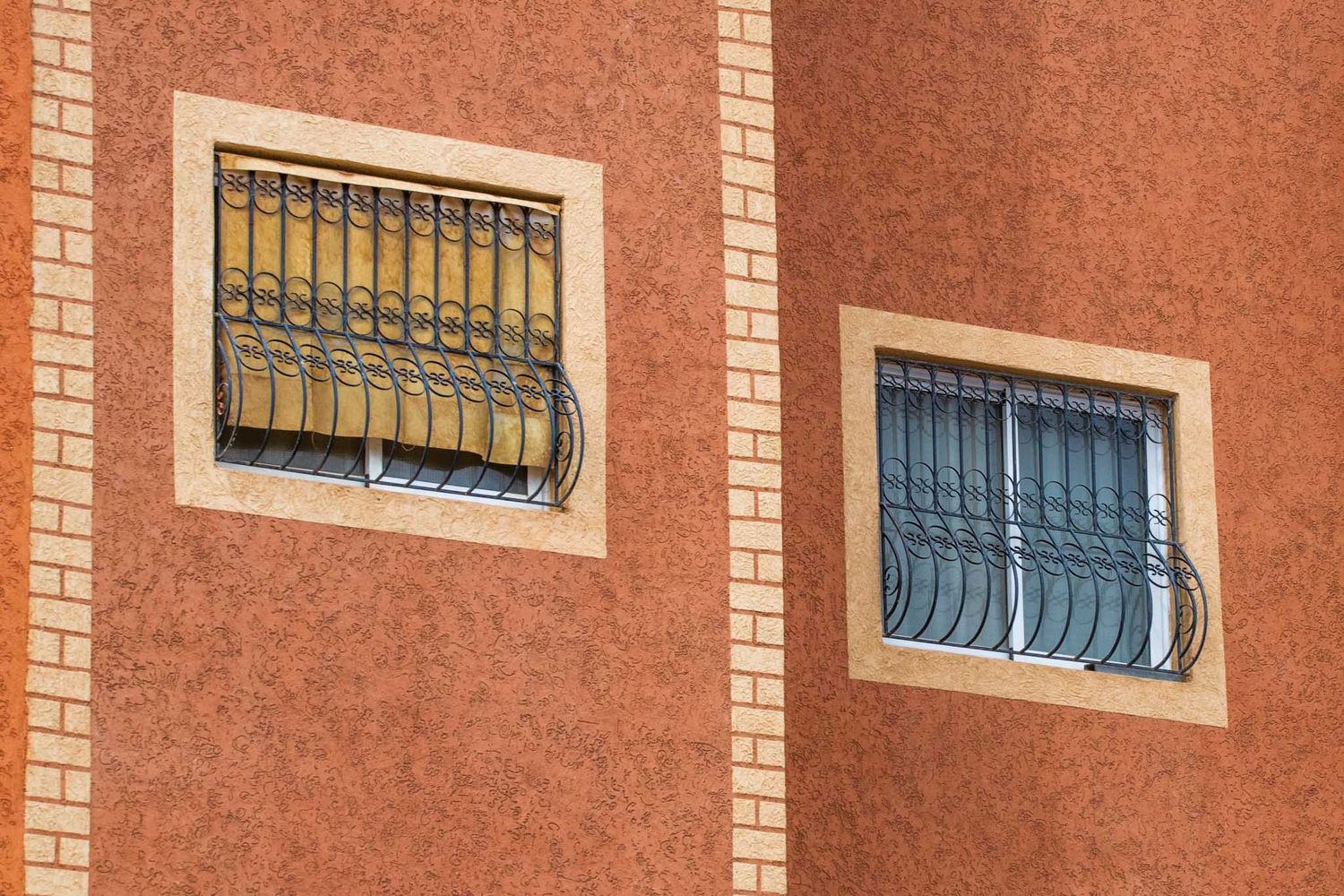 Modern brick building facade with white trim and metal window bars against a blue sky.