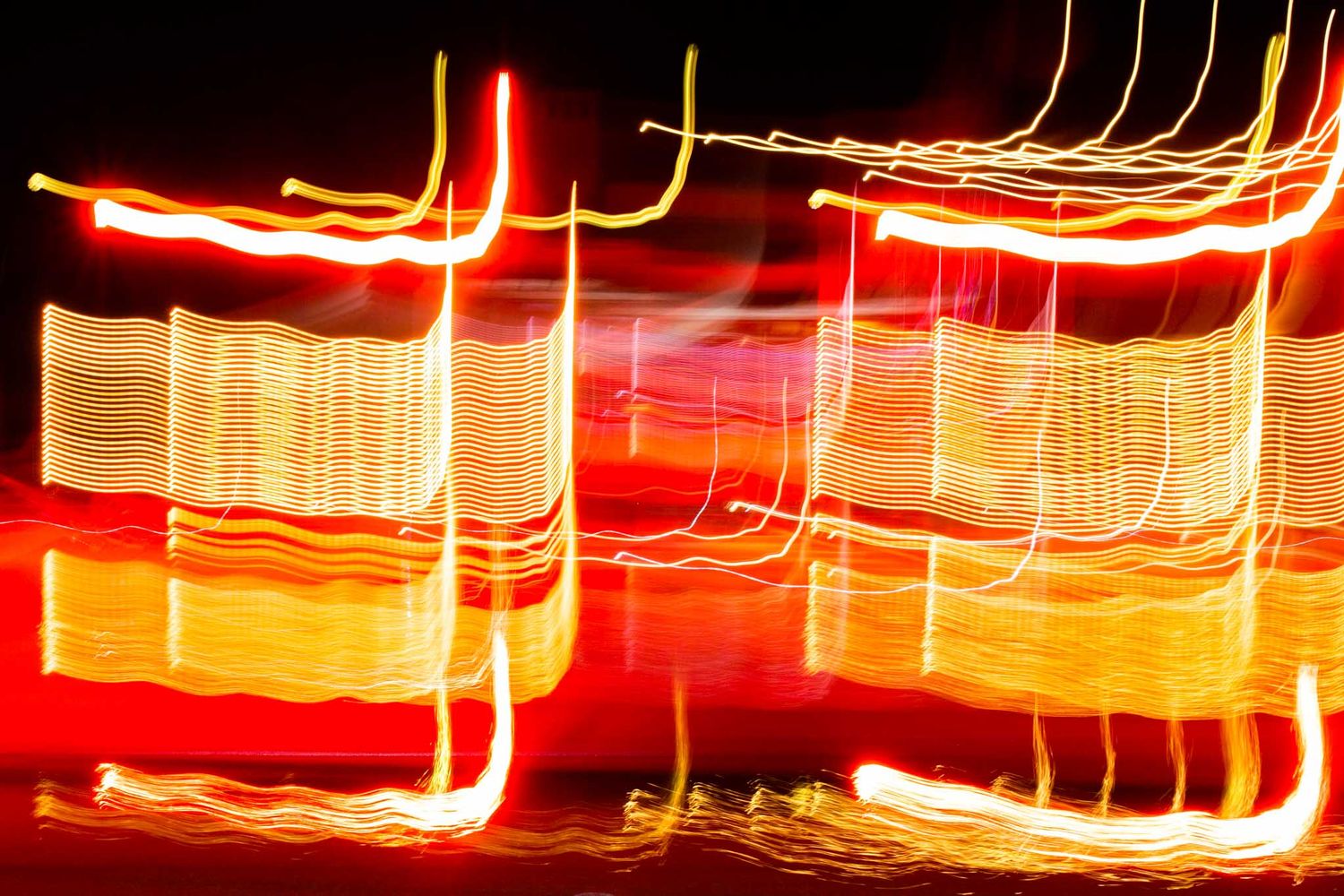 Long exposure photograph shows streaks of red and orange light trails creating abstract patterns against a dark background.