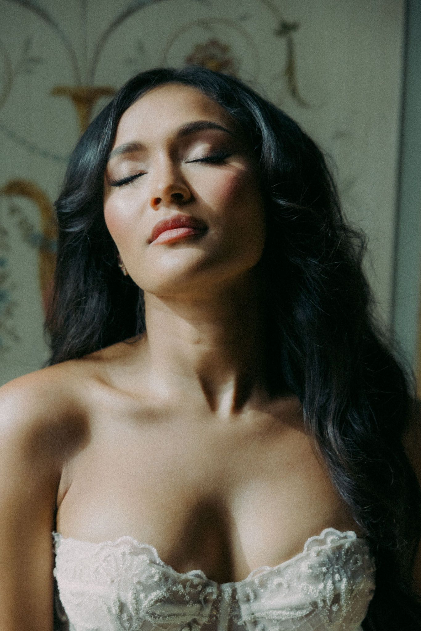 A portrait in soft lighting shows a woman with long dark hair wearing a white lace corset top.
