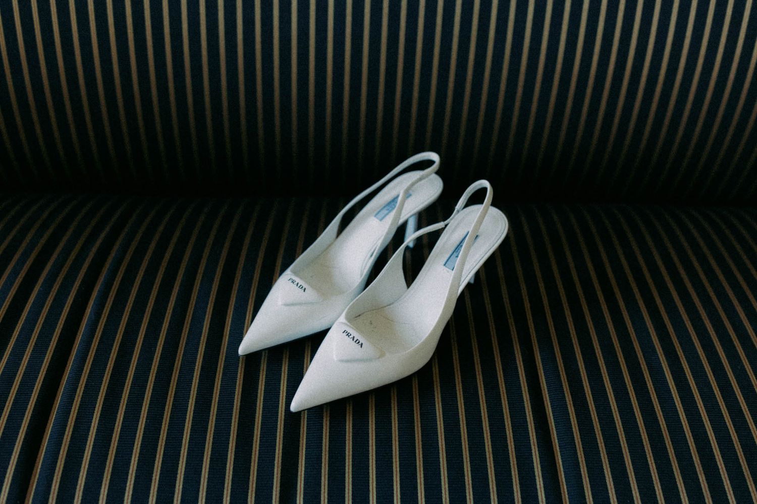 White pointed-toe slingback heels with stiletto heel displayed on striped background.