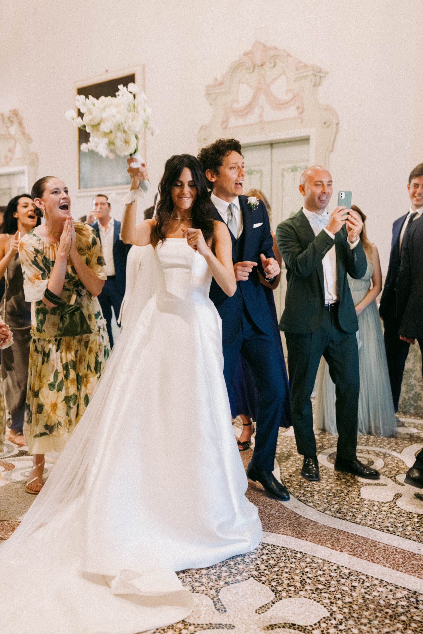 Wedding celebration with couple and guests dancing and celebrating on an ornate tiled floor at an elegant venue.