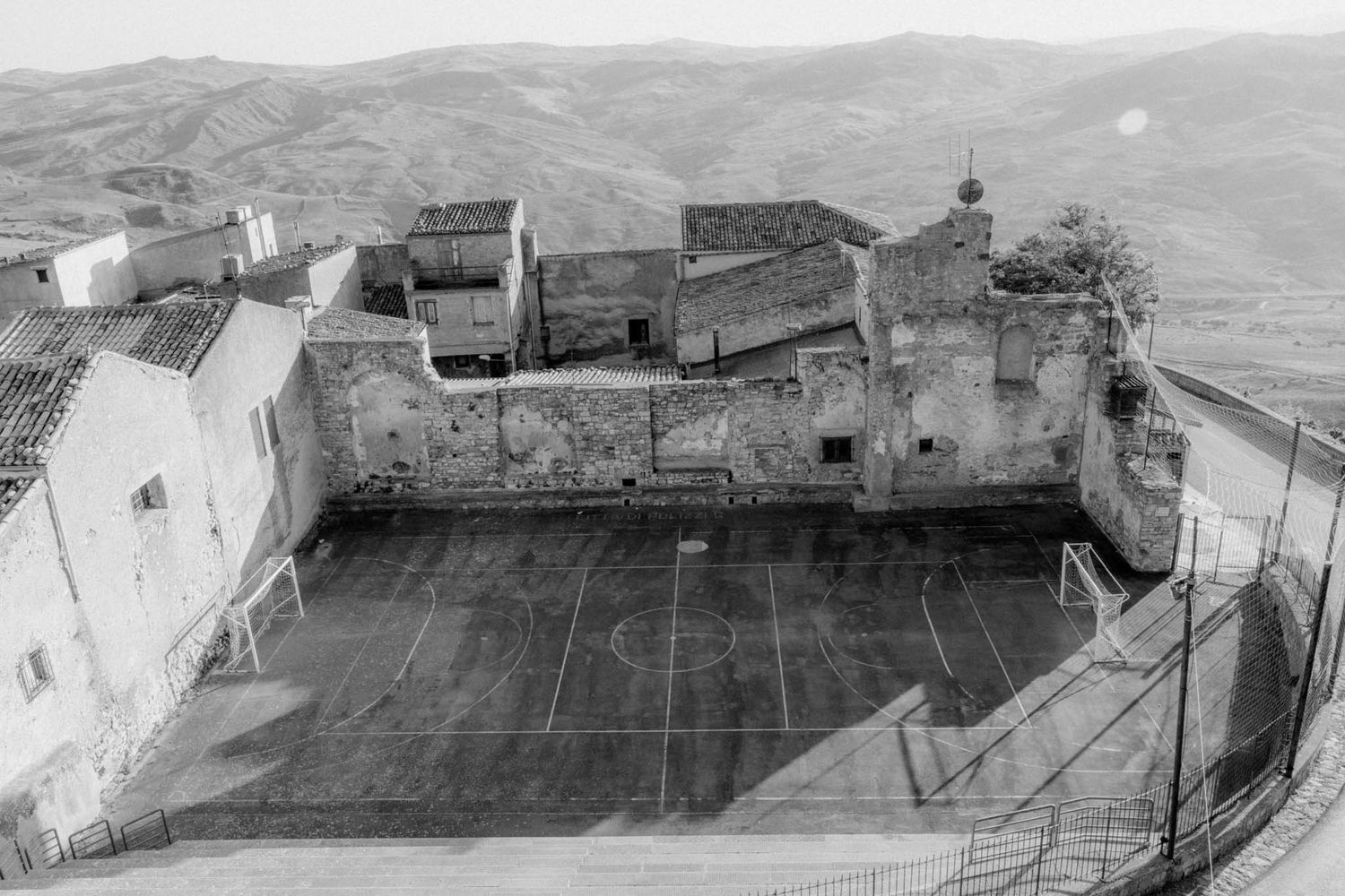 Aerial view of ancient stone buildings and rooftops in a mountainous Mediterranean landscape.