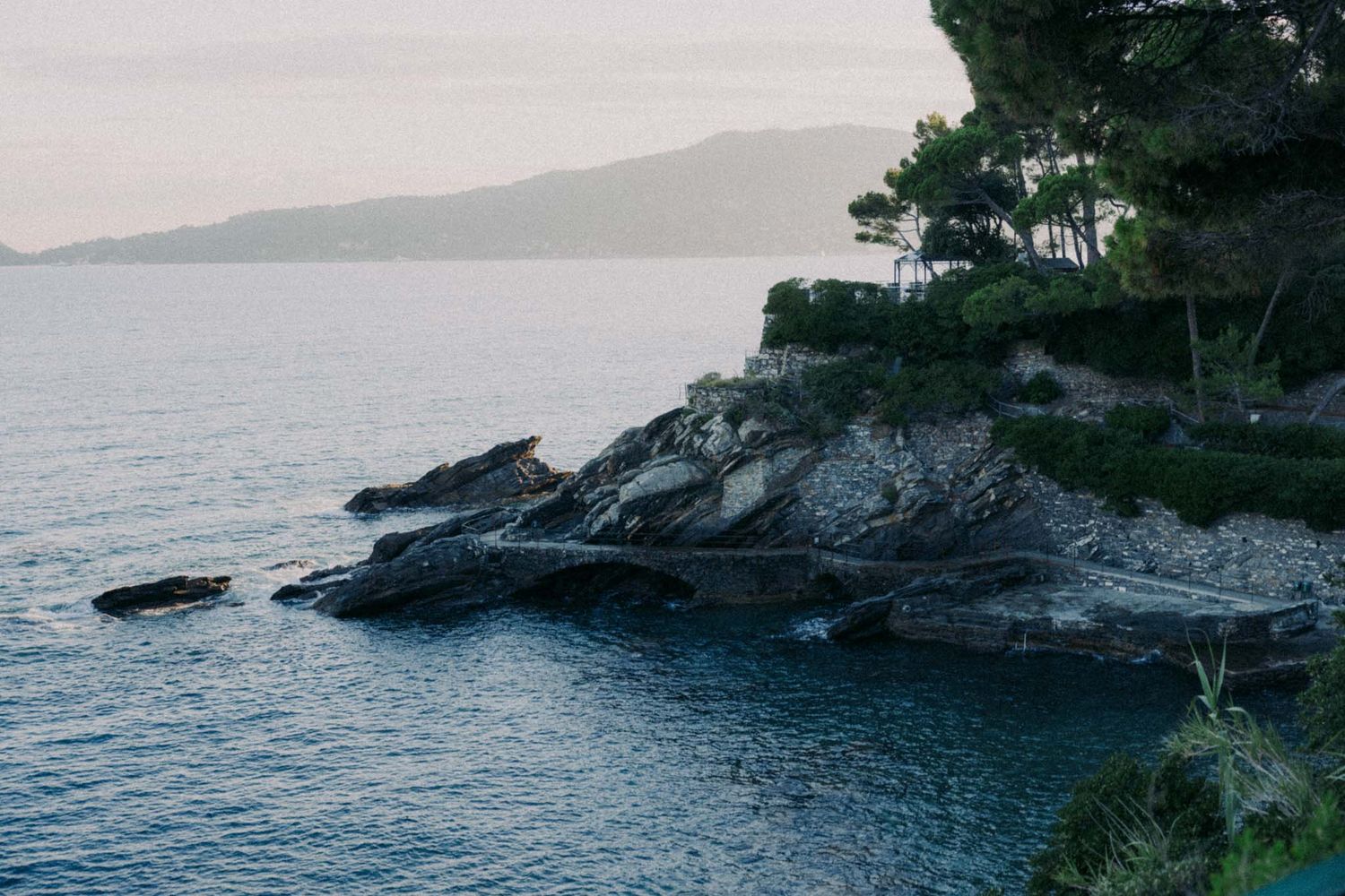 Rocky Mediterranean coastline with rugged cliffs and turquoise waters stretching into the distance at sunset.