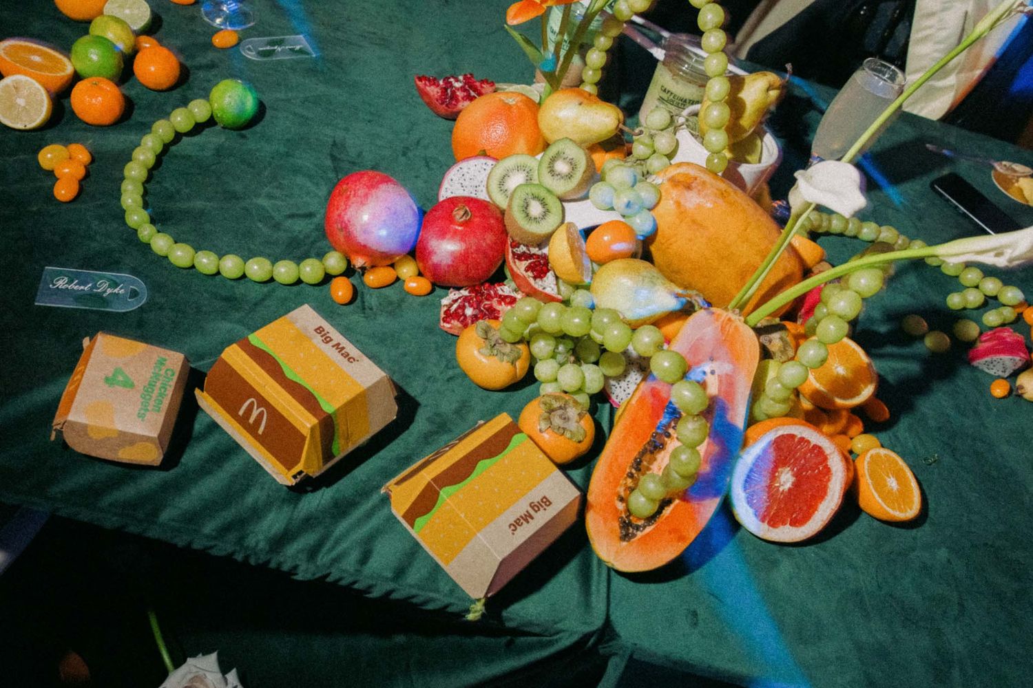 Fresh fruits, vegetables, and packaged snacks scattered on a dark green surface in colorful arrangement.