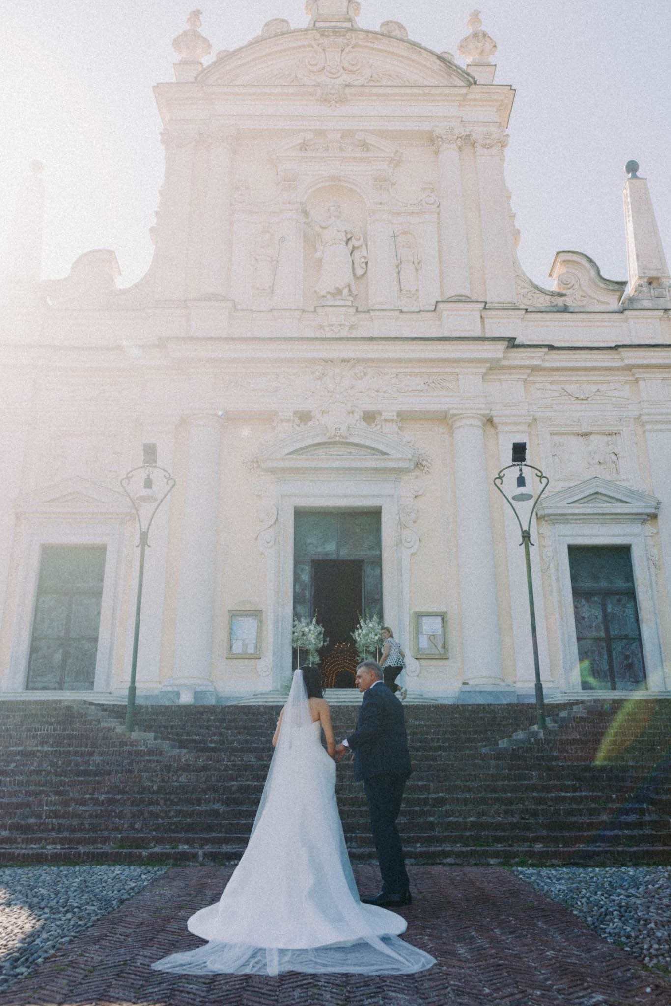 Wedding couple poses in front of a grand white church with stone steps and classical facade.