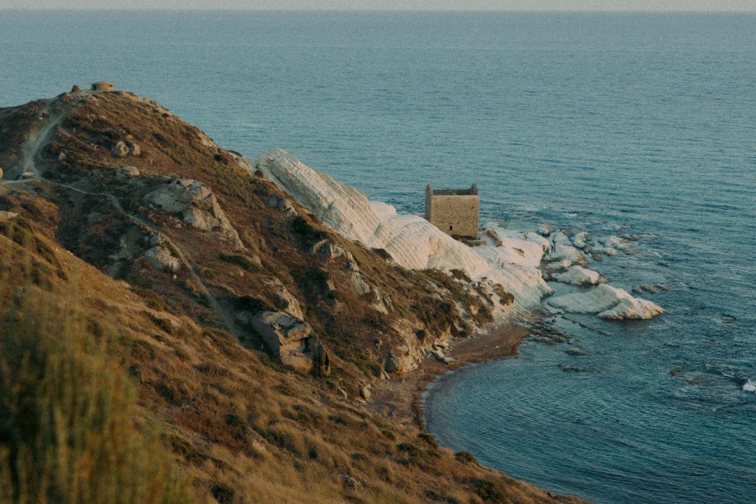Scenic panoramic view of a rugged coastline with cliffs and blue ocean waters during golden hour.