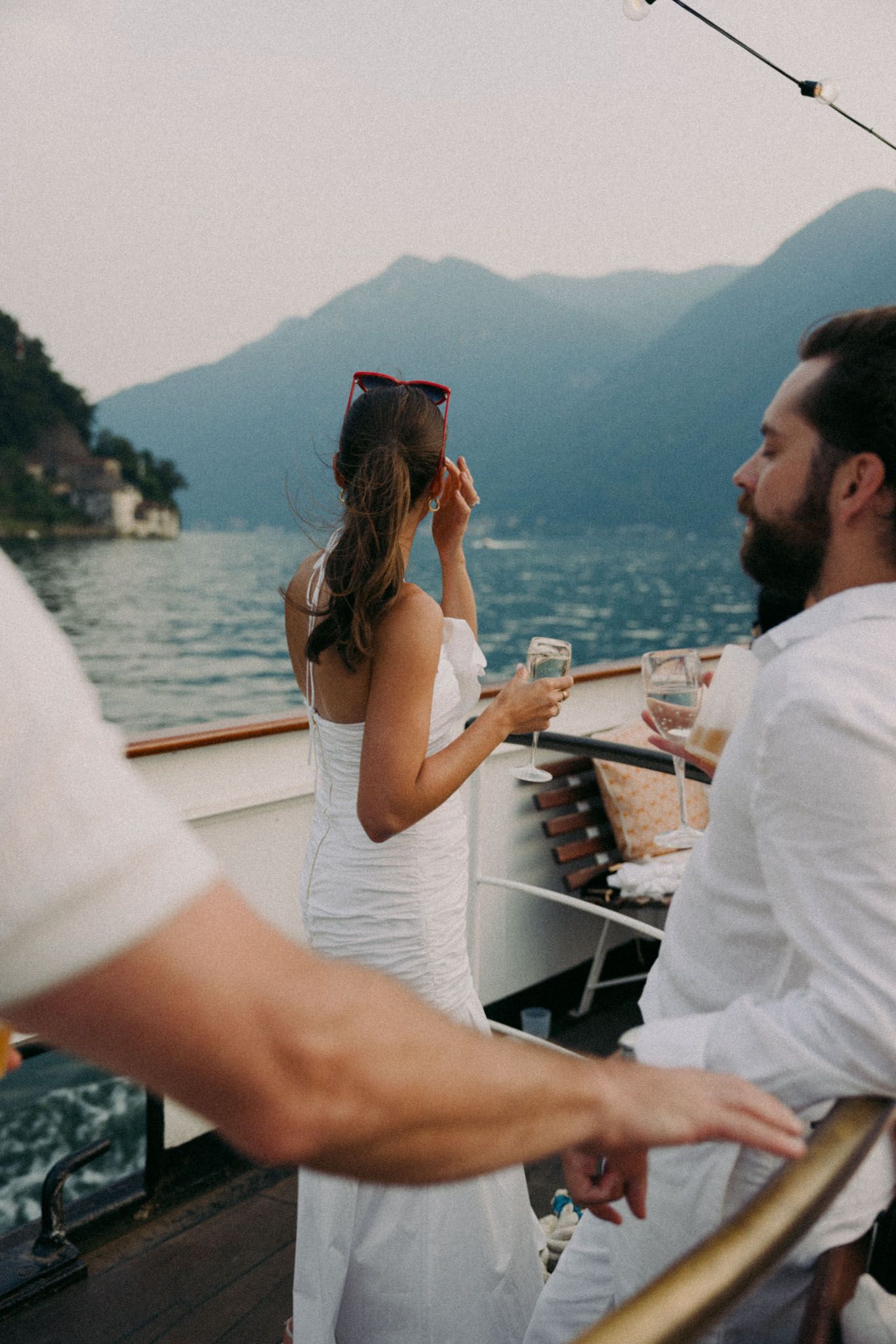 A couple enjoys drinks and conversation on a boat with scenic mountain views across the lake at sunset.