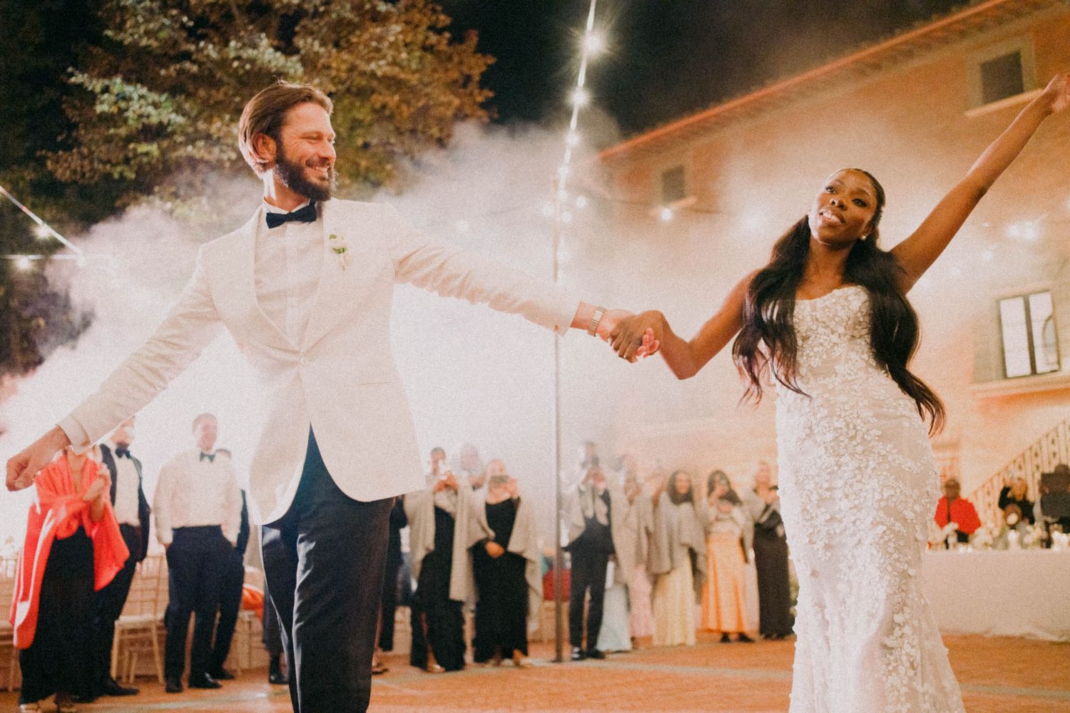 Couple shares a joyful moment during their first dance at an elegant evening wedding reception with sparklers.