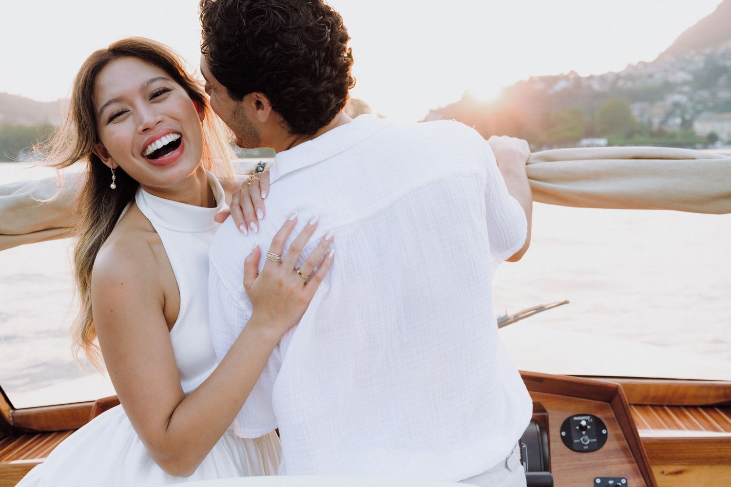 A couple shares an intimate moment laughing together on a boat during sunset.