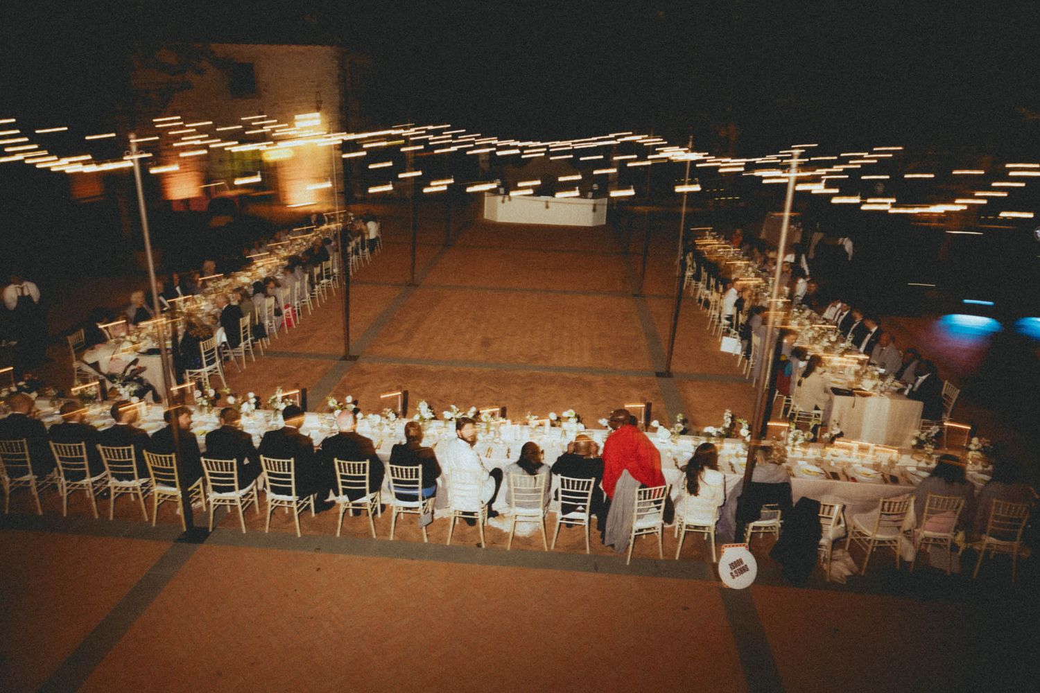 String lights illuminate a rustic wedding reception venue with long tables and chairs set up for dining.