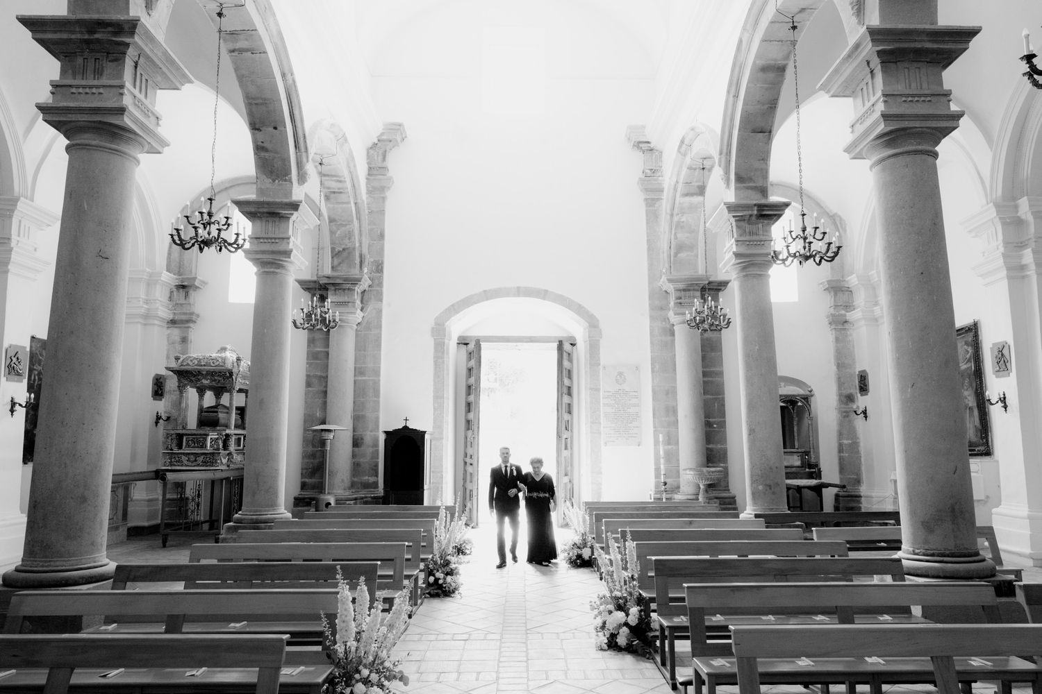 Interior view of a historic church with white columns and arches illuminated by natural light through windows.