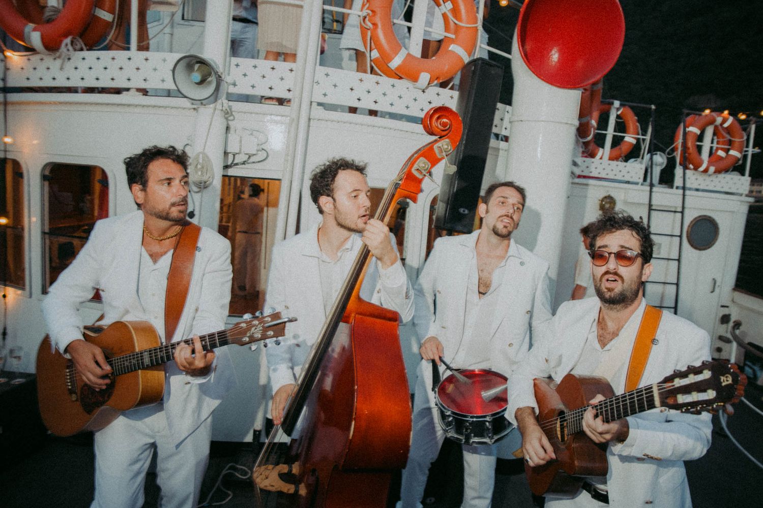 Musicians perform together in a lively jam session with acoustic instruments and red lighting accents.