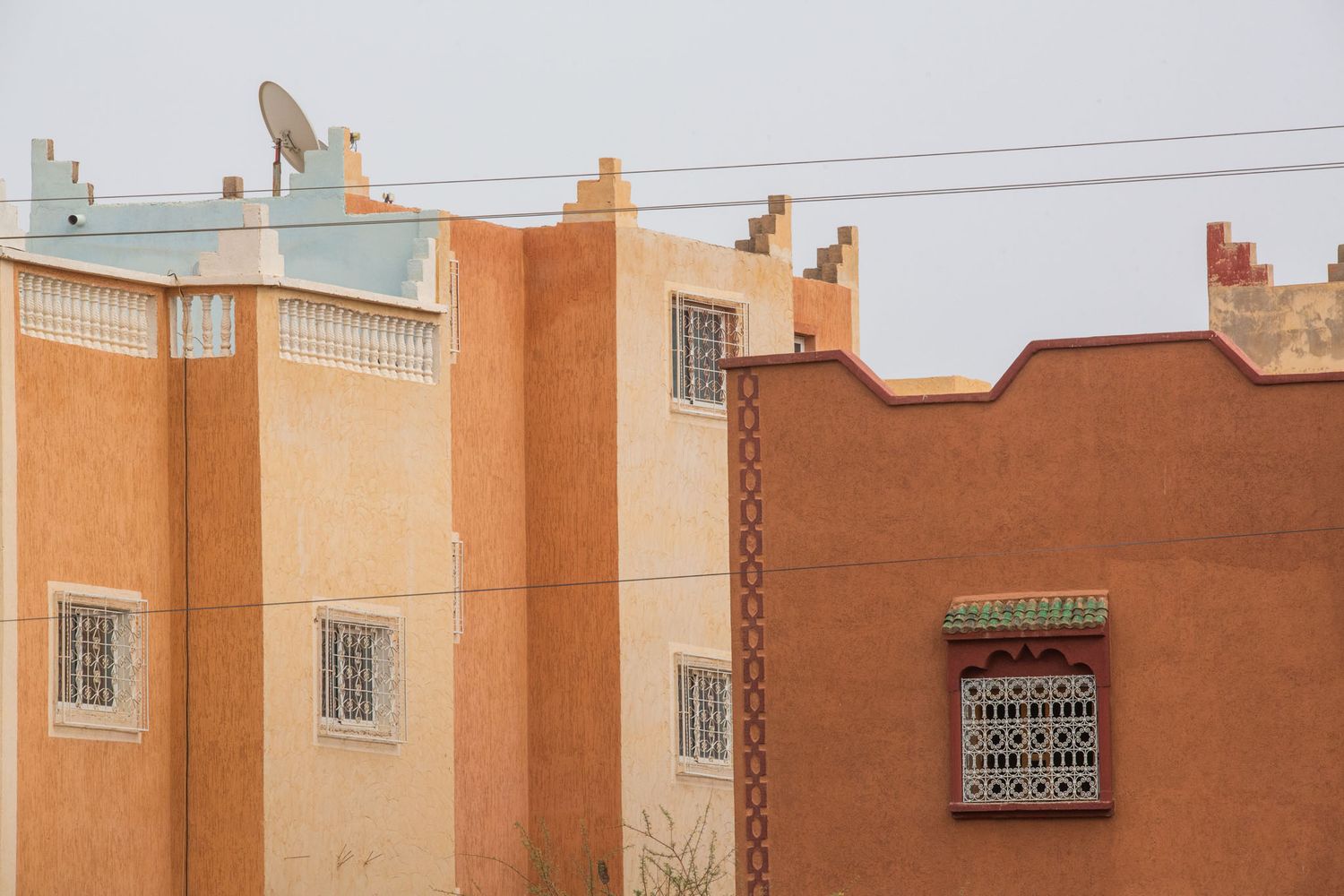 Row of terracotta-colored buildings with traditional Moroccan architectural features and power lines overhead.
