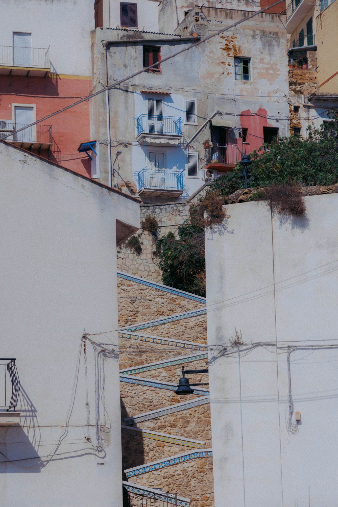 Zigzagging staircase on white and pink Mediterranean buildings with small balconies and weathered walls.