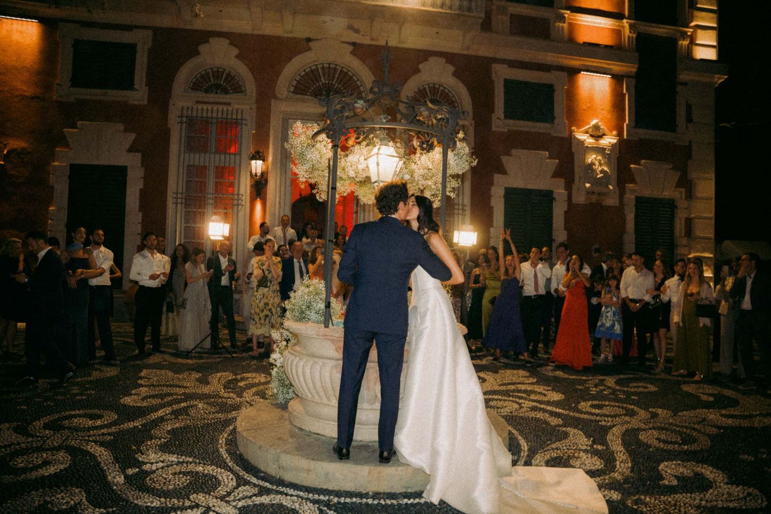 Elegant evening wedding reception in a grand ballroom with ornate chandeliers and classical architecture.