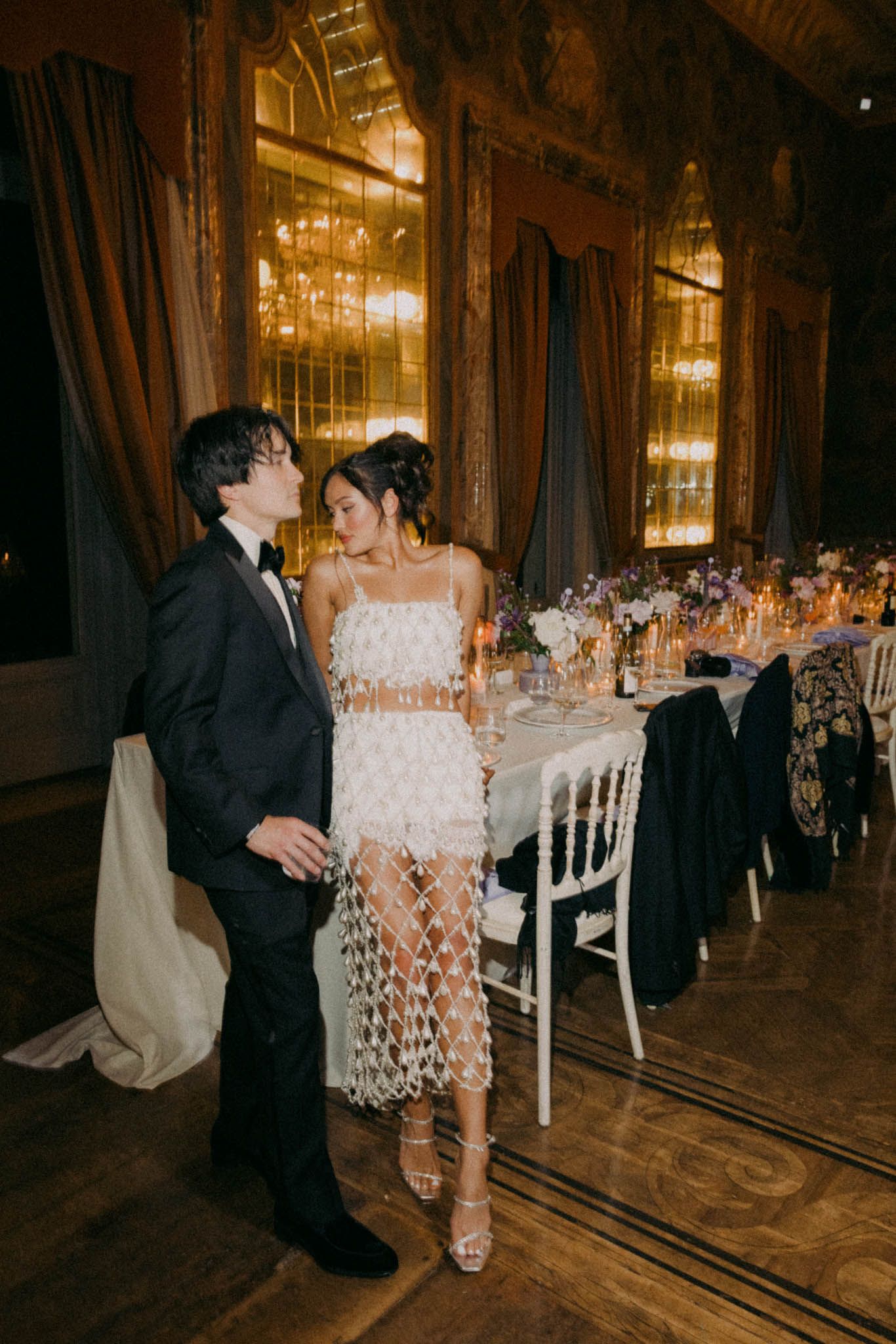 A couple shares a romantic dance moment in an elegant ballroom with ornate chandeliers and table settings.